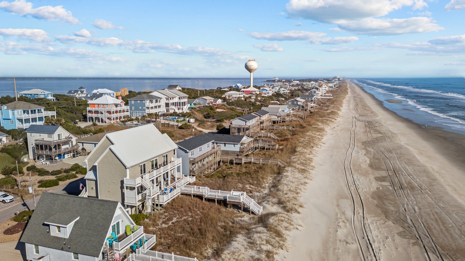 Aerial view of beachfront vacation homes along pristine sandy shoreline with water tower landmark visible.