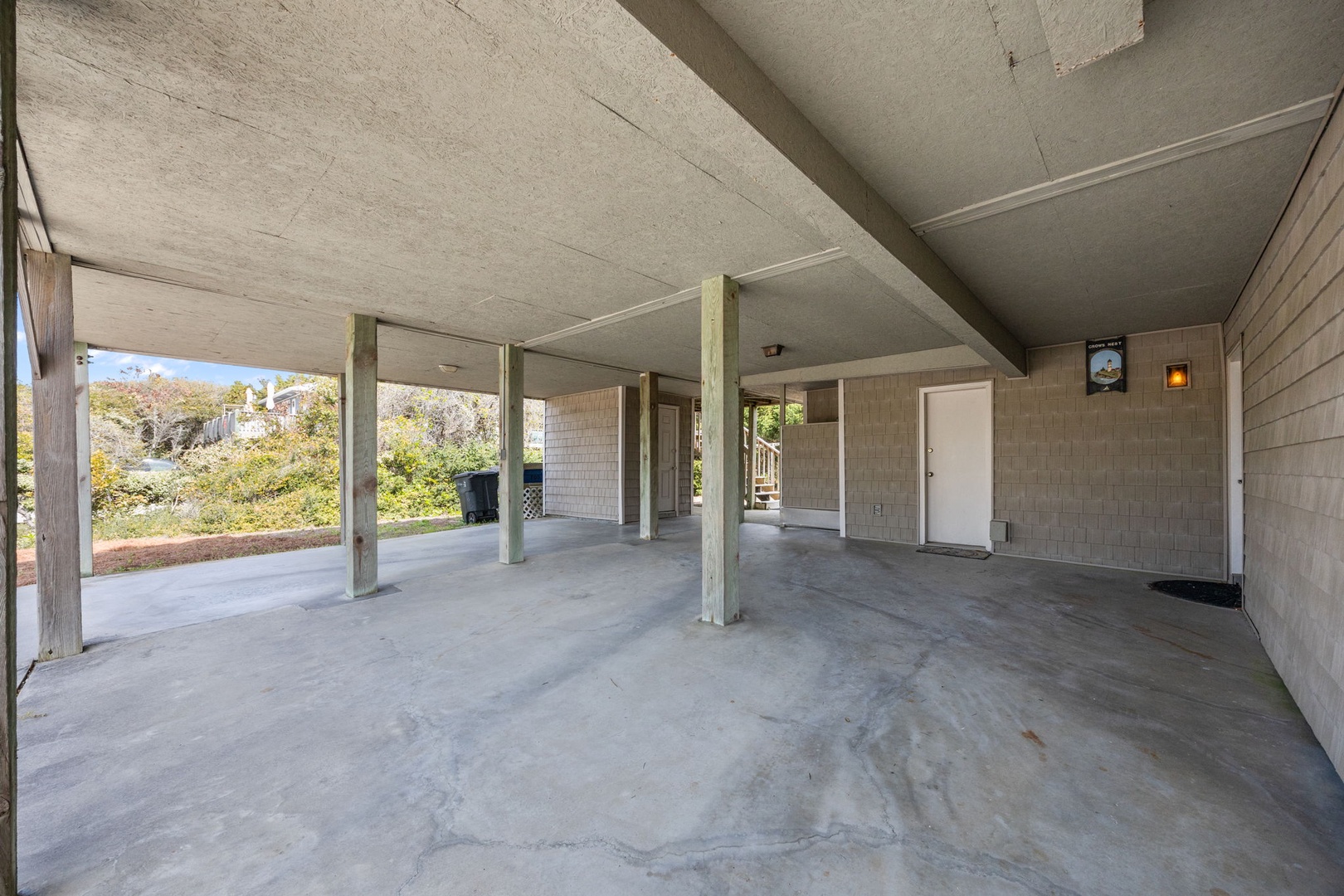 Spacious covered parking area with concrete flooring and support beams, featuring easy access to the property entrance and natural surroundings.