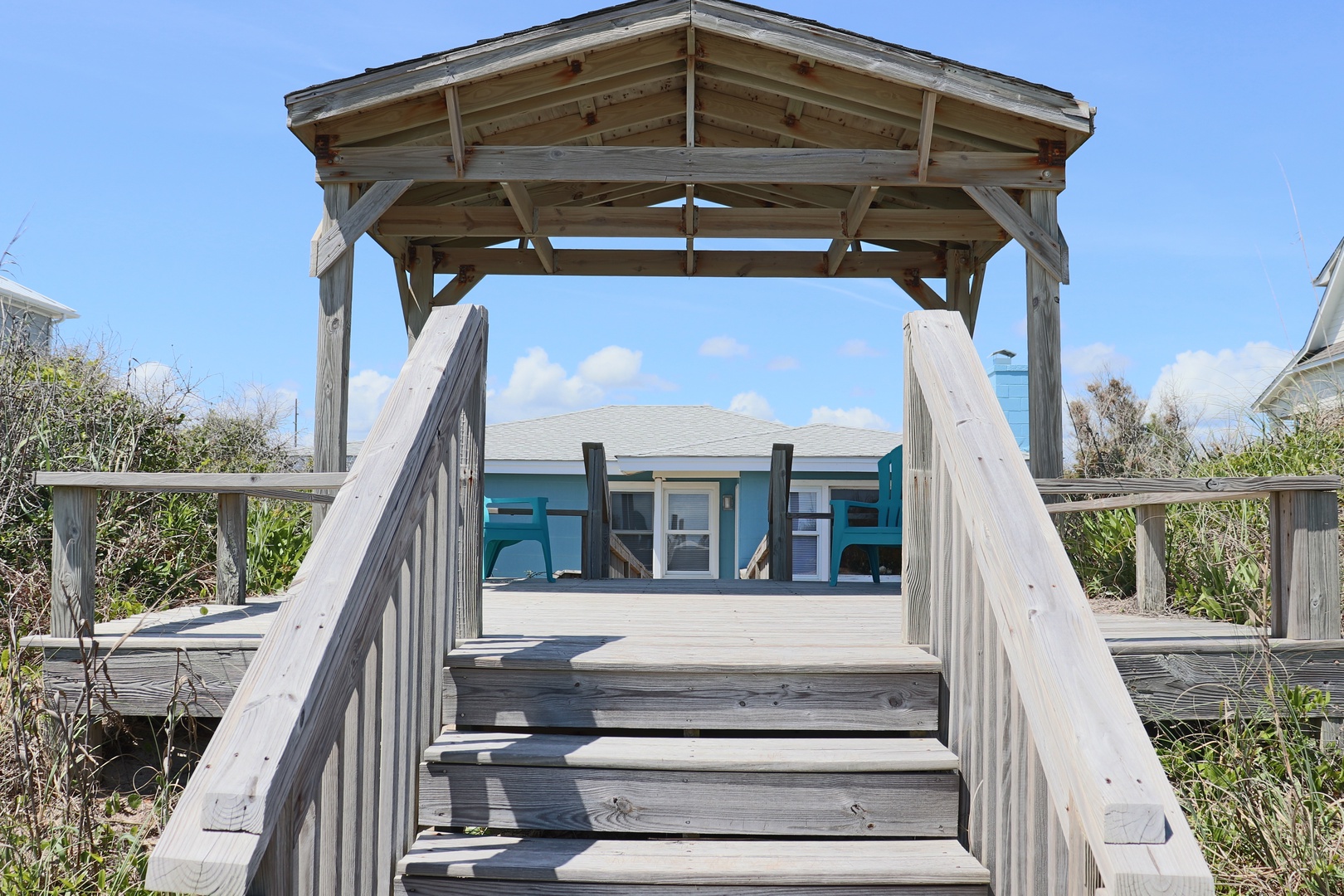 Charming beach house with weathered wooden walkway and coastal architectural details set among natural dune vegetation.