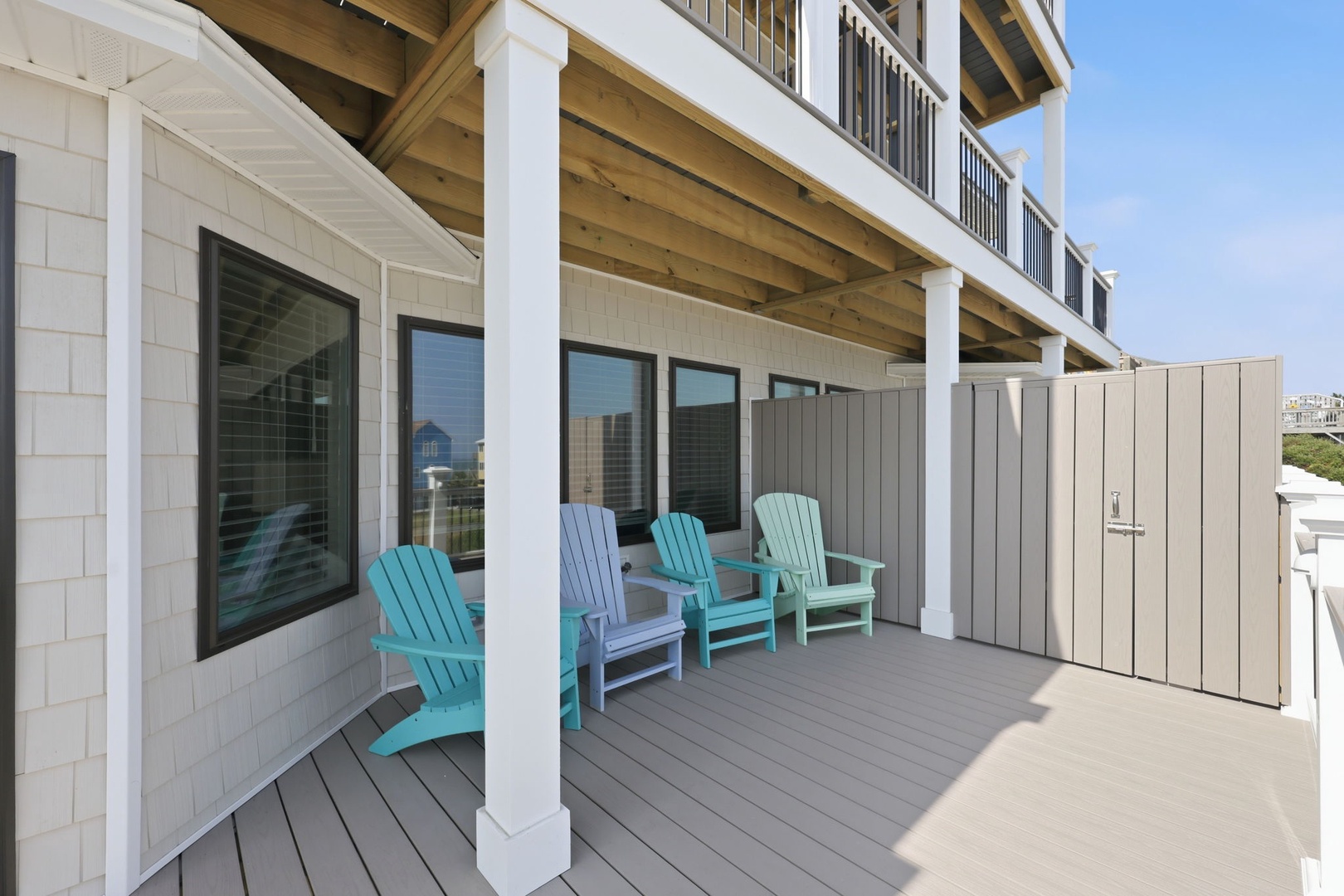 Your private covered deck awaits with colorful Adirondack chairs, perfect for morning coffee or sunset cocktails in this breezy coastal retreat.