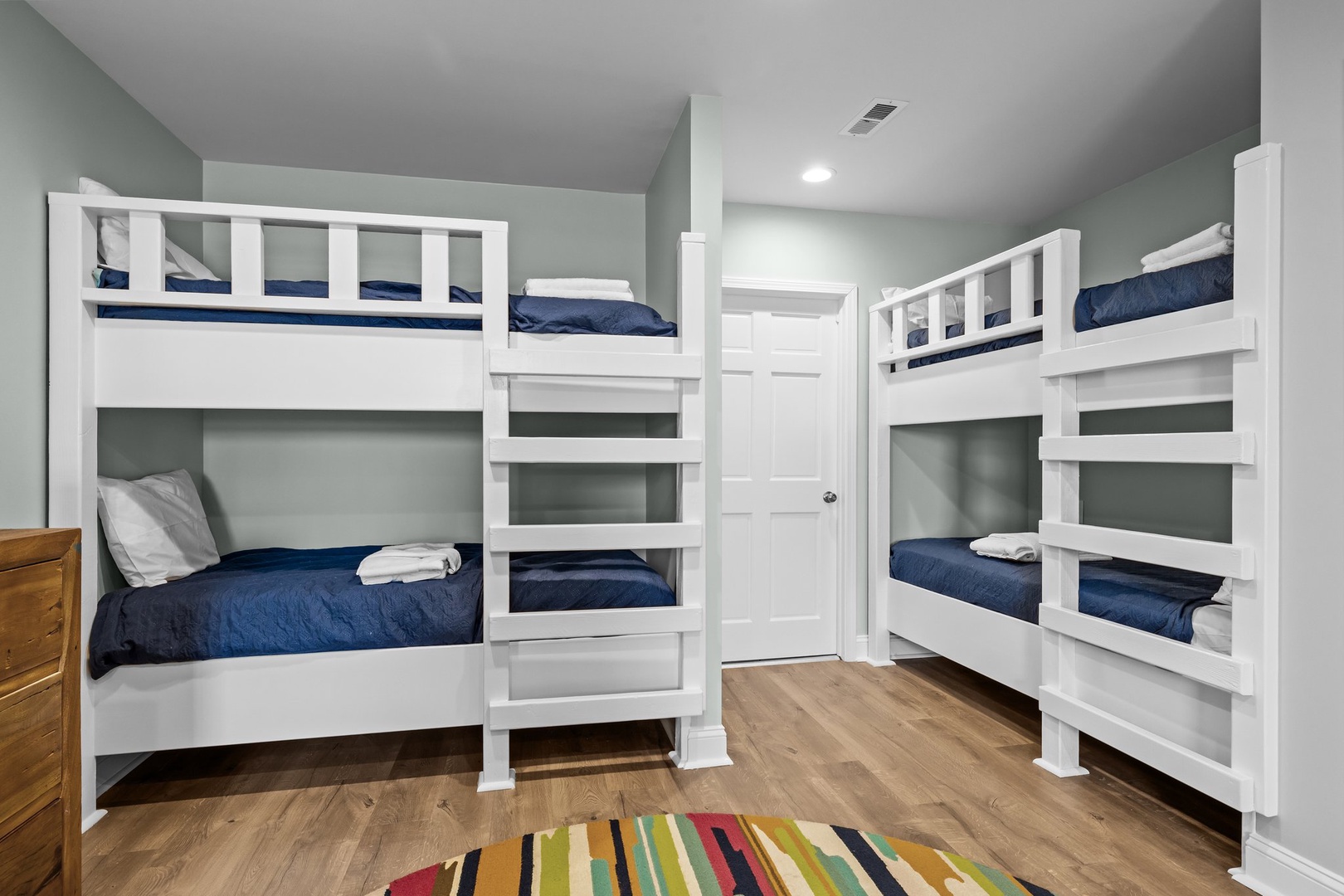 Your group will love this cozy bunk room with two sets of sturdy white beds, complete with navy linens and colorful striped rugs for comfort.