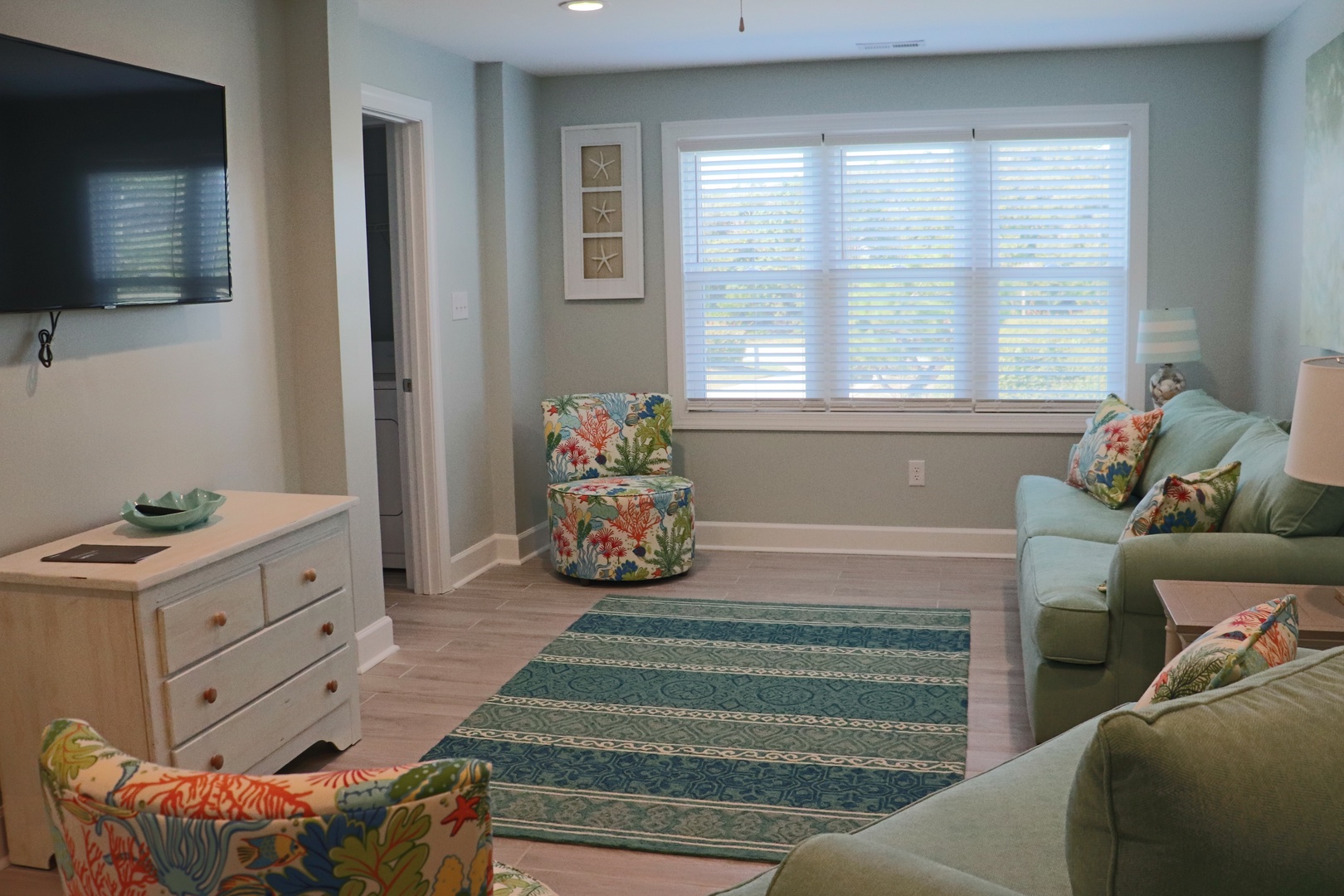 Unwind in your bright, coastal-themed living room with comfortable seating, natural light, and cheerful tropical accents perfect for relaxing.