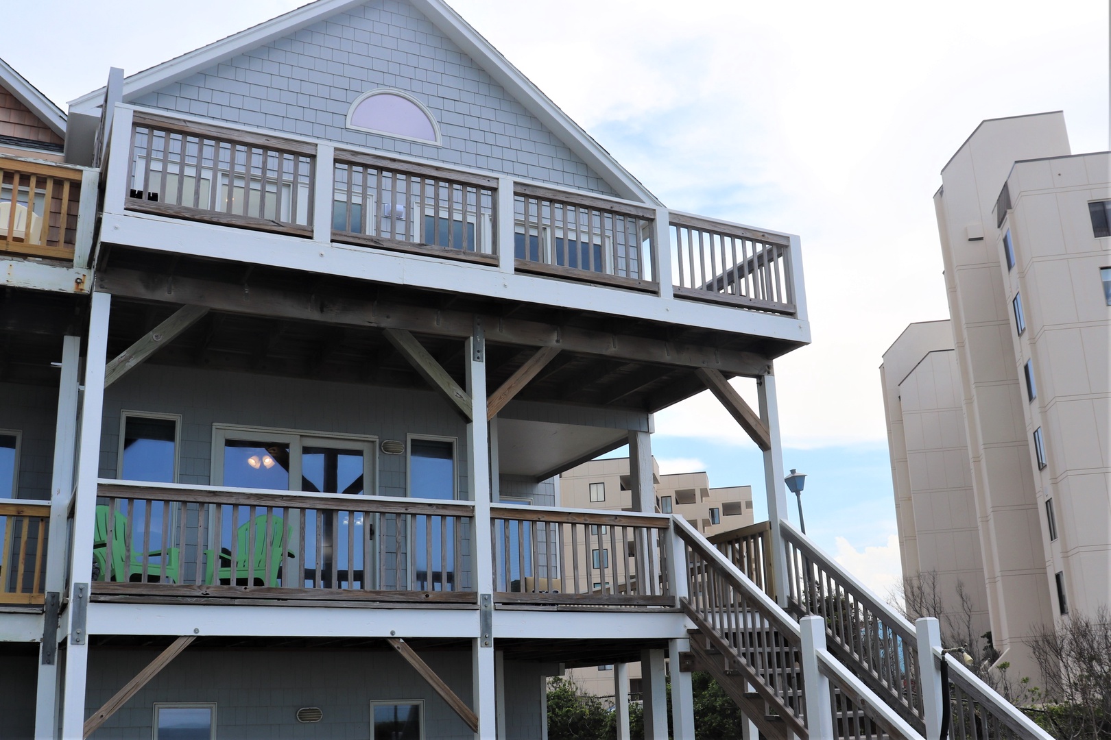 A distinctive blue coastal cottage with wraparound deck featuring green Adirondack chairs and elevated design perfect for ocean breezes.