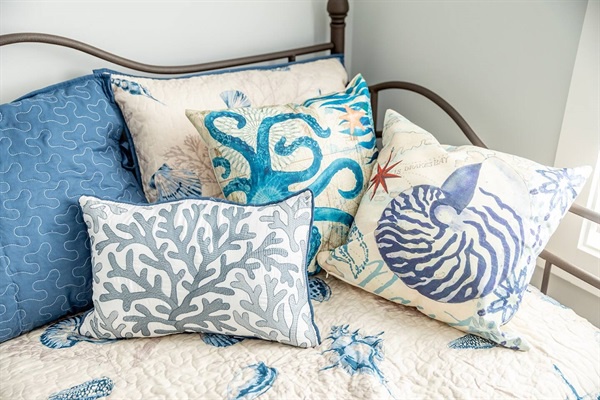 Ocean-themed pillows create coastal comfort on your bed, featuring seahorses, coral, and nautilus shells in soothing blues.