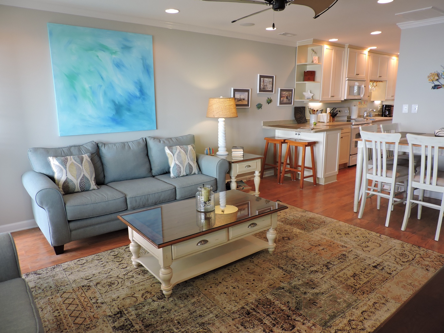 Relax in your bright open-concept living space with coastal artwork, comfortable seating, and a fully equipped kitchen perfect for preparing meals.
