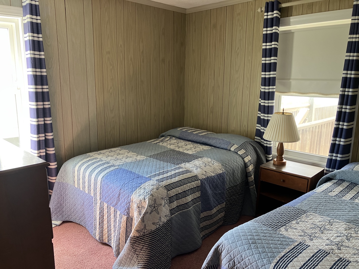 Settle into your cozy twin bedroom where nautical quilts and warm wood paneling create the perfect coastal retreat atmosphere.