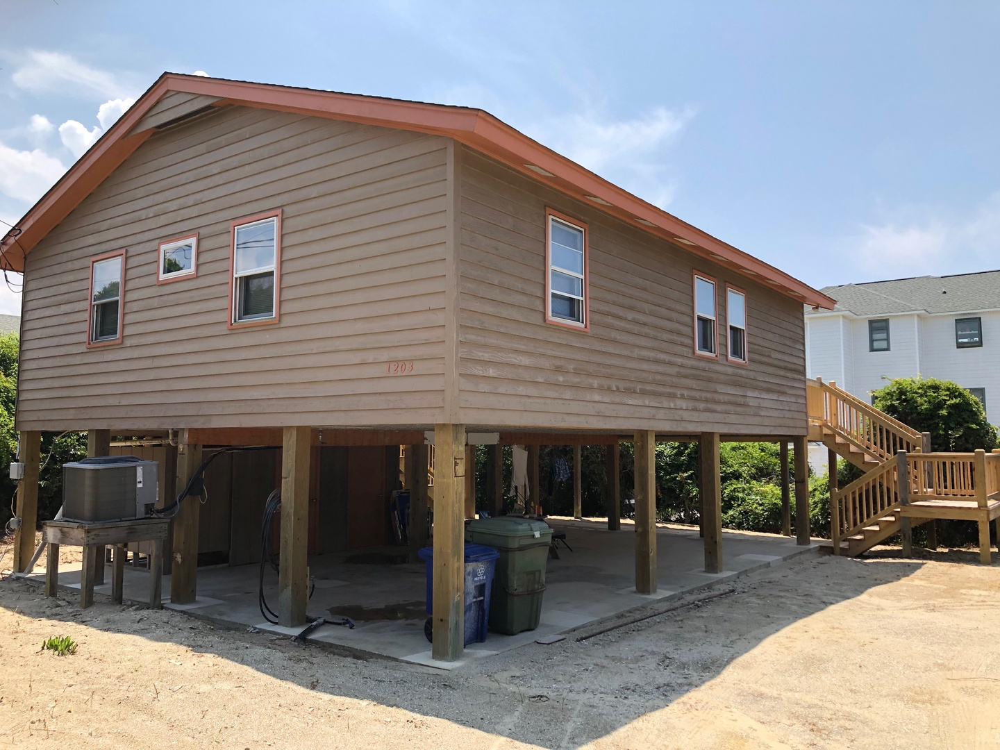Elevated beach house features covered parking and wooden stairs leading to your coastal getaway.