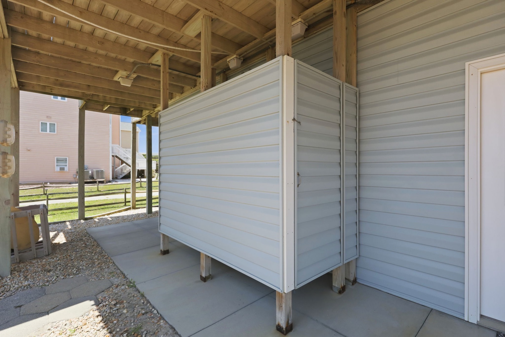 A covered outdoor storage area with a practical enclosed unit, positioned beneath the home on stilts—ideal for beach gear, surfboards, or outdoor equipment near the coast.