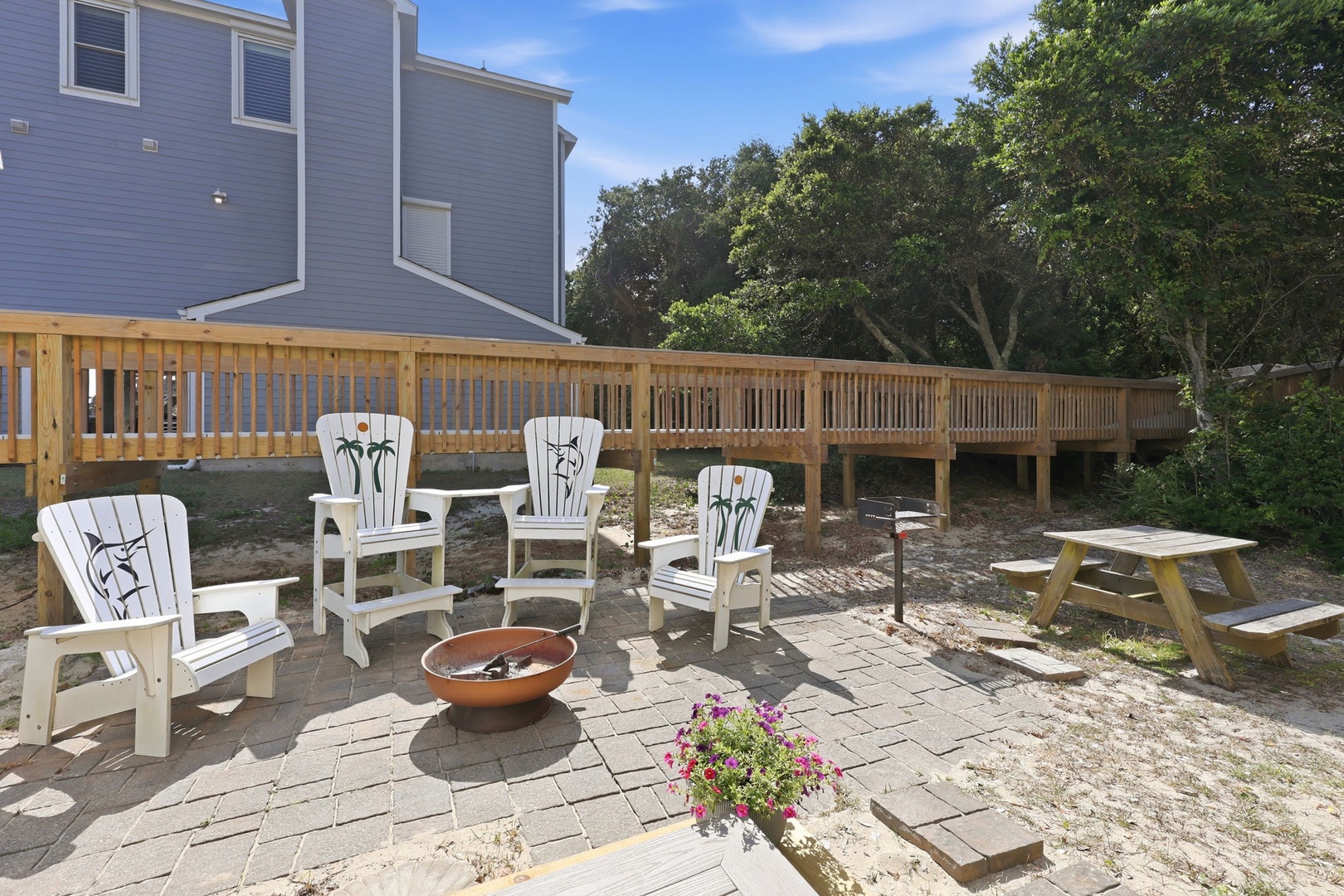 A charming outdoor retreat features Adirondack chairs around a fire bowl, with a picnic table ready for alfresco meals. The spacious deck and mature trees create a peaceful backdrop for gathering.