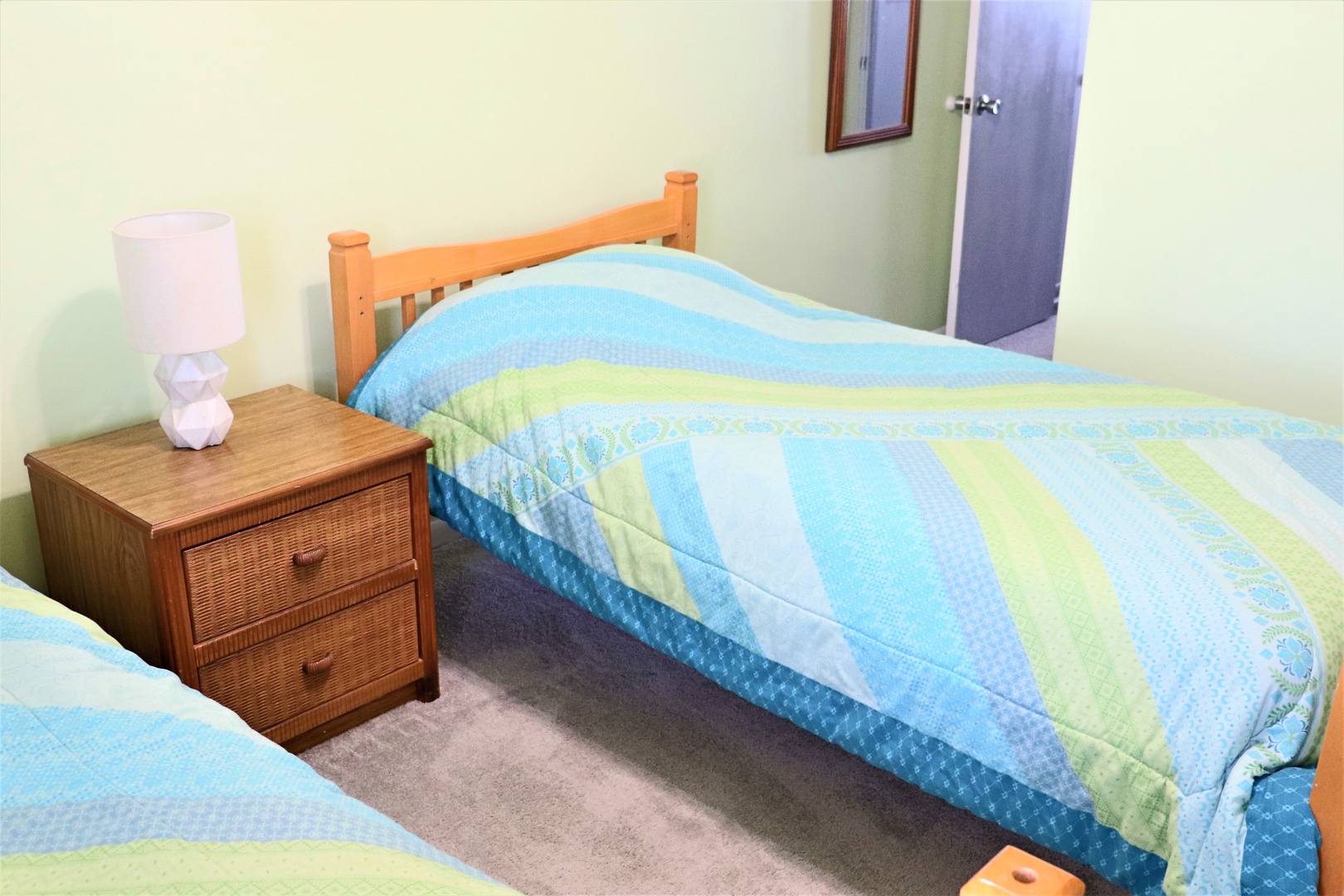 Drift off peacefully in your cozy twin bedroom, featuring comfortable beds with cheerful blue and green linens and warm wood furnishings.