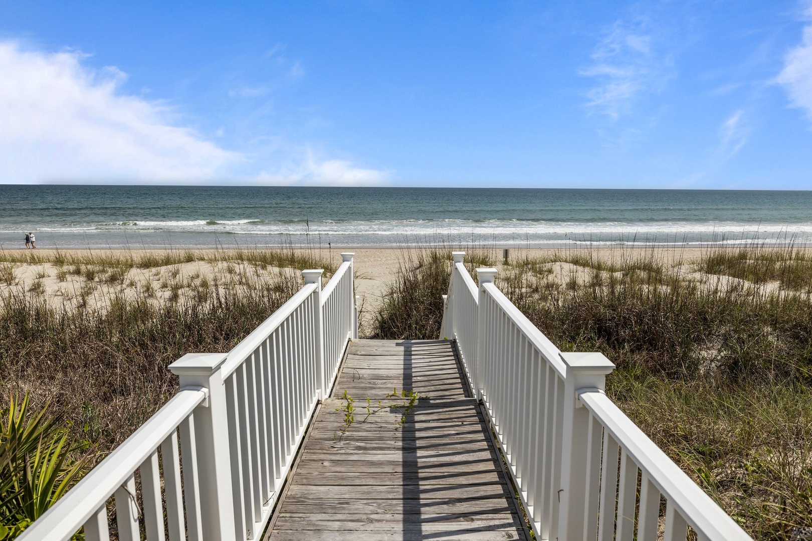 Private beach access via wooden boardwalk leading directly to pristine sandy shores and ocean waves.