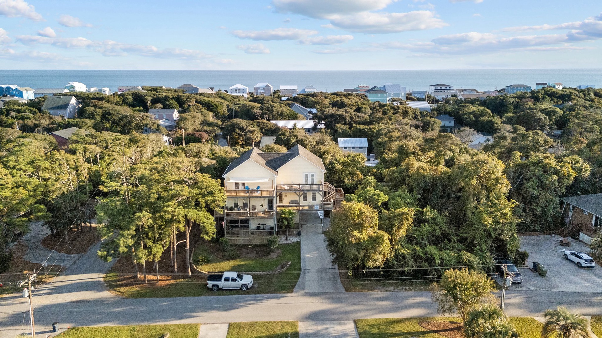 Elevated coastal home surrounded by mature trees near beach, with multiple homes dotting the wooded shoreline community.