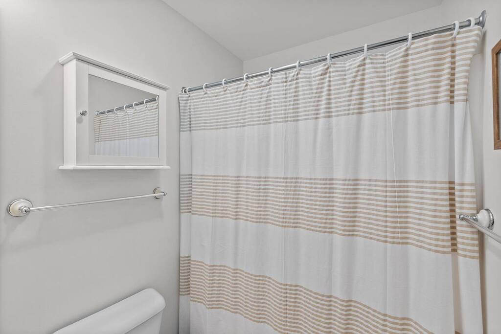 Step into your spotless bathroom featuring a spacious shower with elegant striped curtains and thoughtful touches for your comfort.