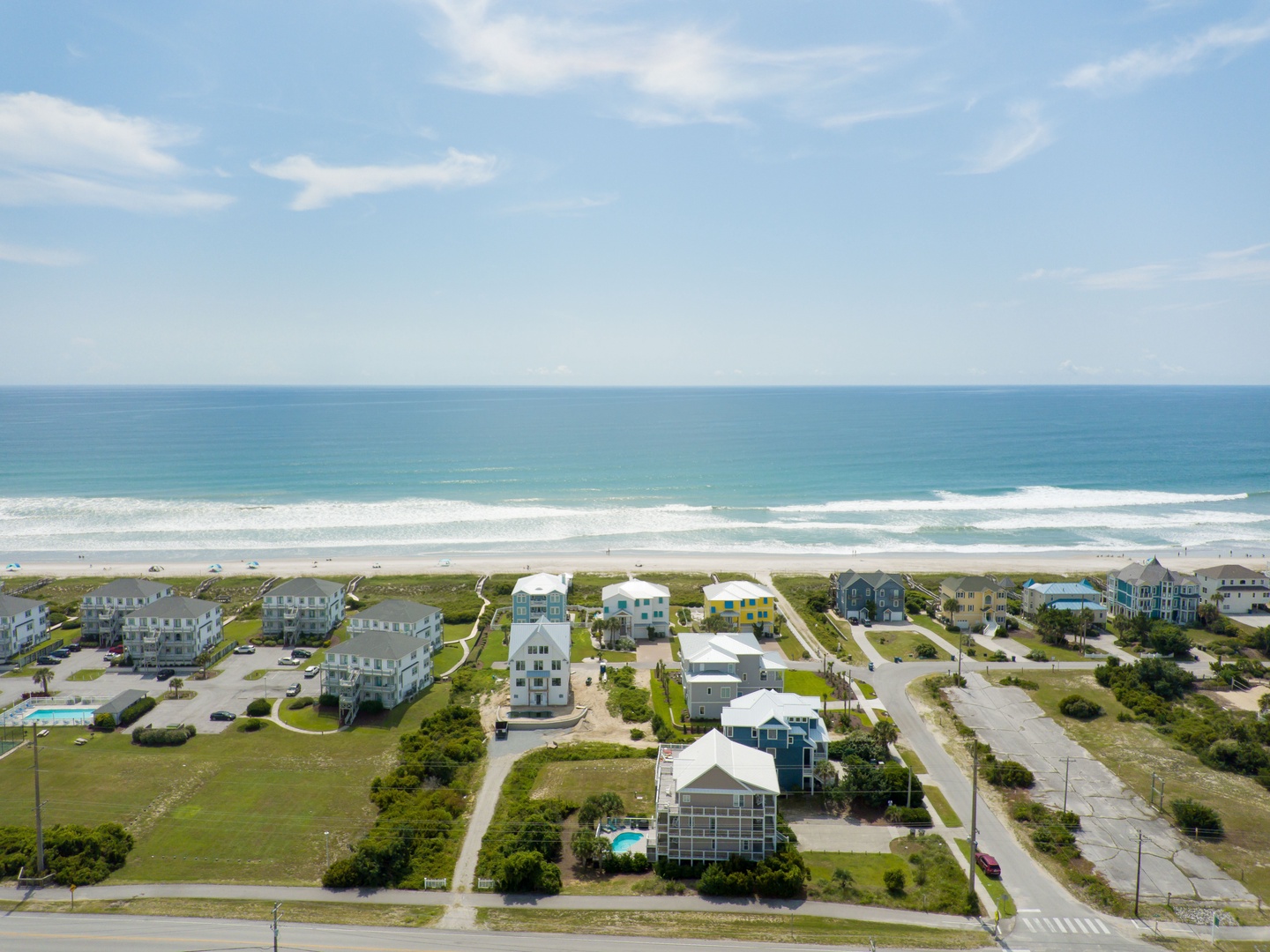 Aerial view of beachfront vacation rentals nestled between rolling green dunes and pristine ocean shoreline.