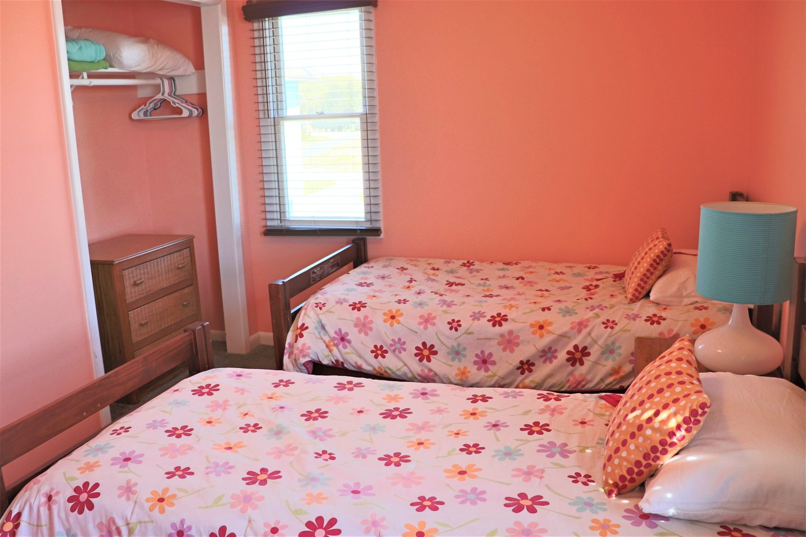 Your cheerful bedroom features twin beds with vibrant floral bedding, built-in storage, and natural light streaming through.