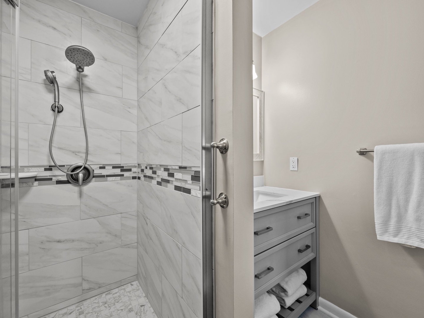 Refresh in your stylish marble-tiled shower with modern rainfall head and sleek glass enclosure.