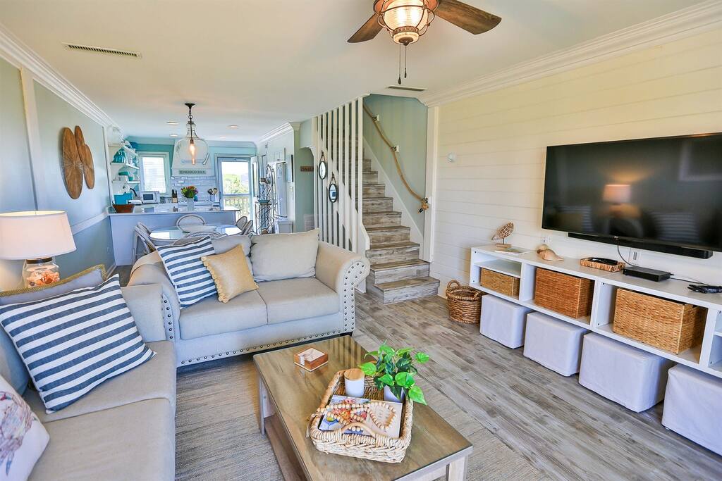 Unwind in your coastal living room featuring nautical touches, a large TV, and built-in storage with wicker baskets.
