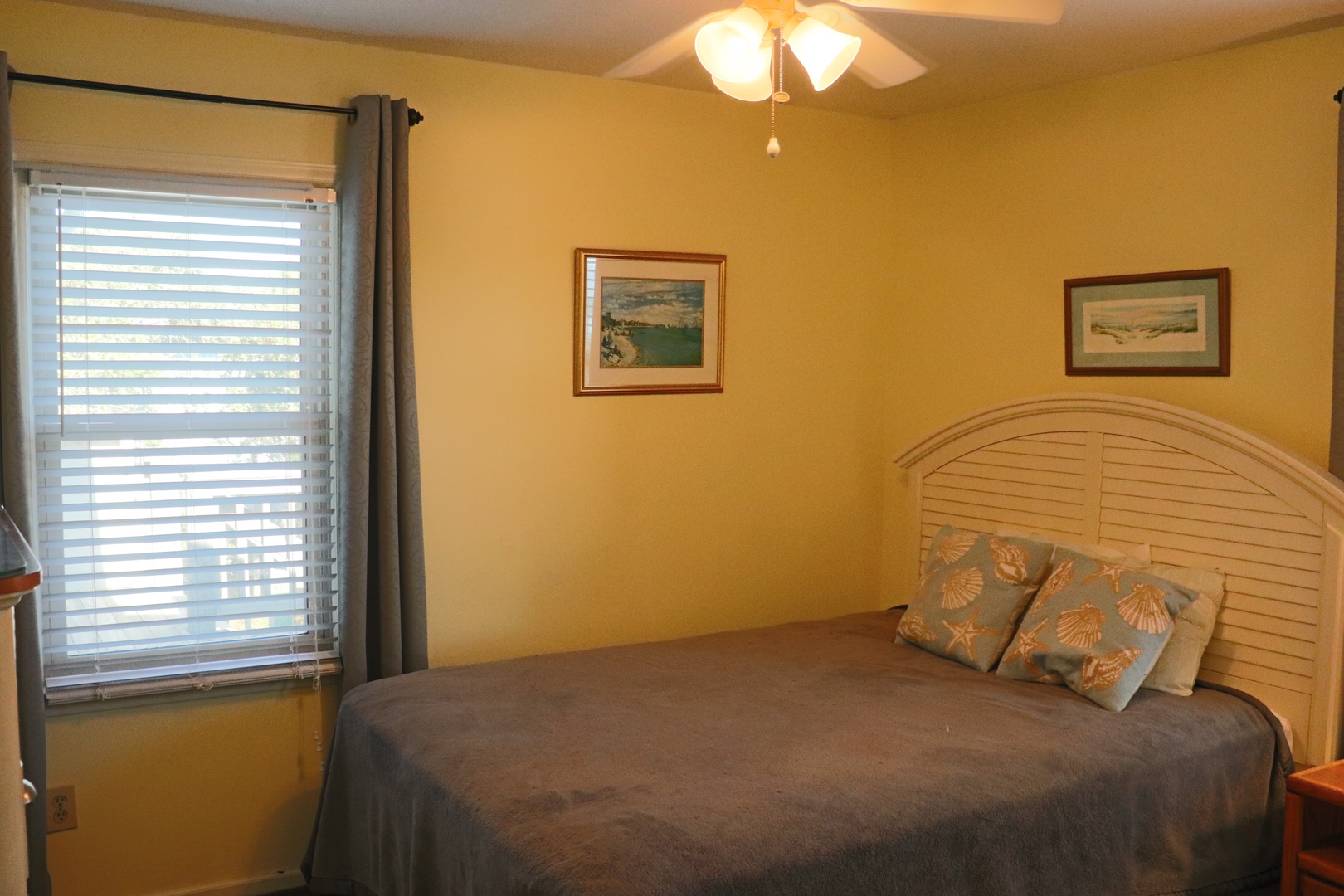 Drift into restful sleep in this cozy bedroom with warm yellow walls, coastal artwork, and gentle natural light.