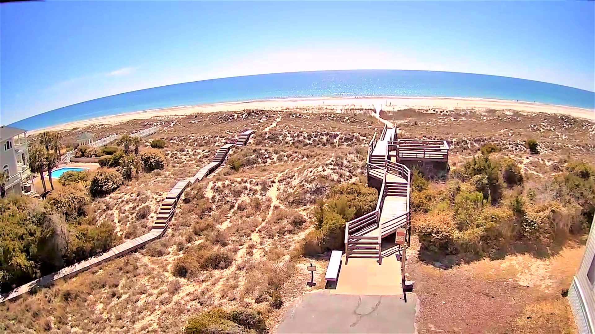 Spectacular aerial view showcasing the expansive coastline and elevated wooden walkways leading through natural dunes to the pristine beach below.