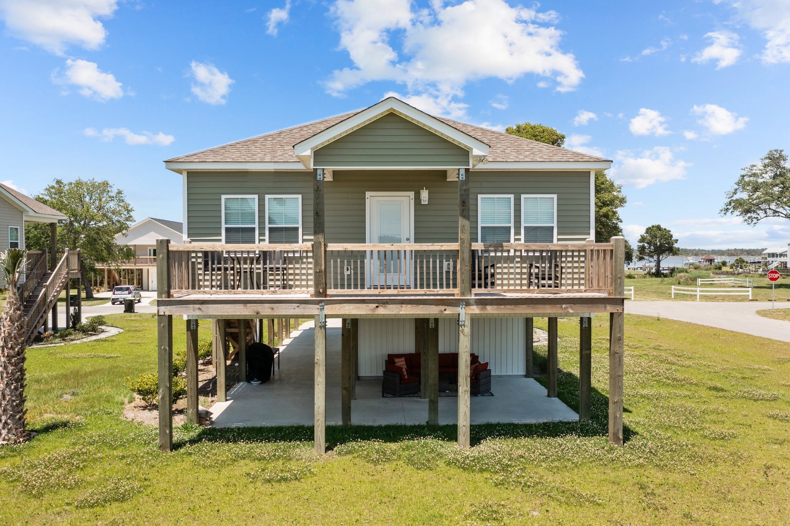 Elevated coastal home featuring covered parking and wraparound deck with water views in the distance.