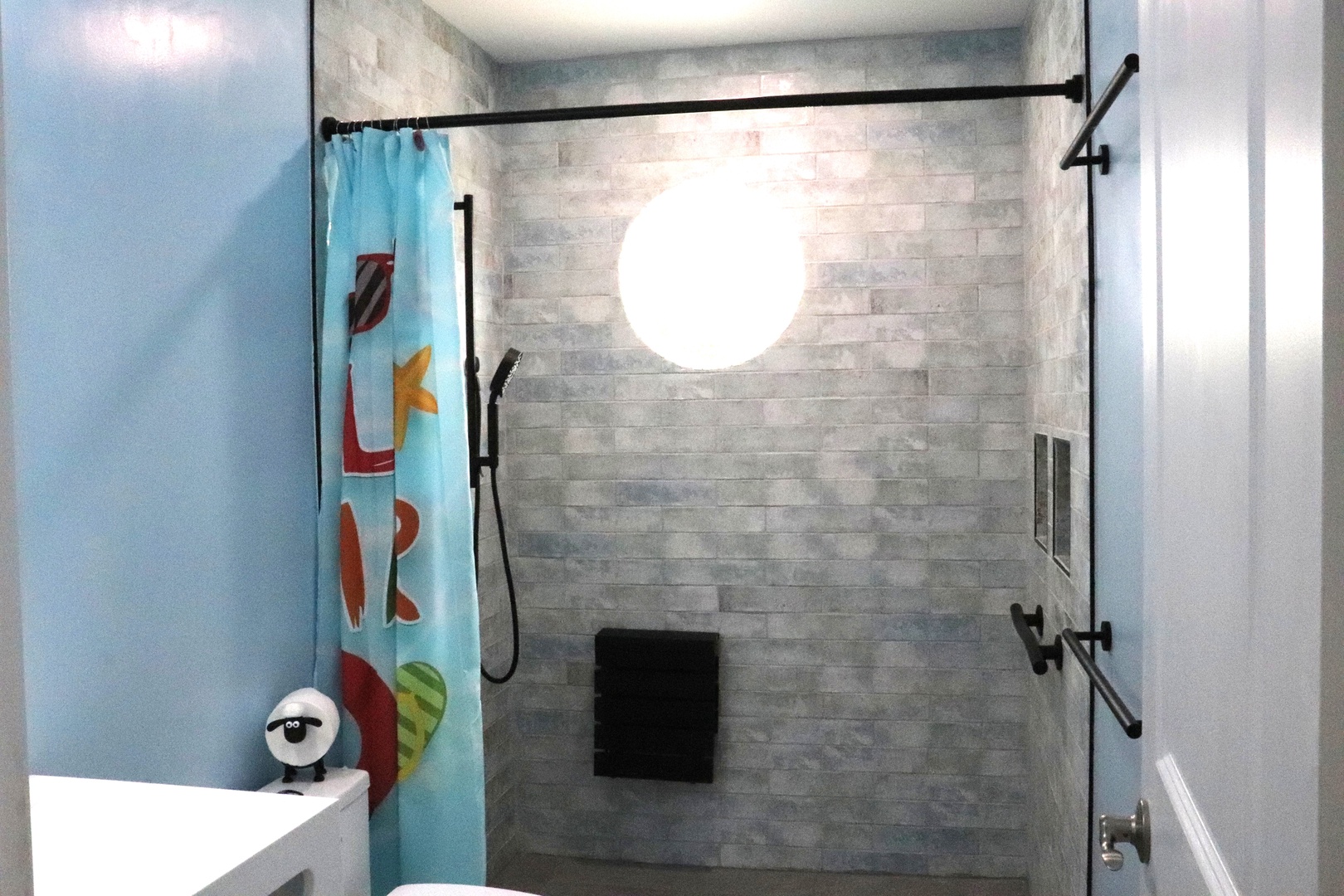 Step into your private spa-like shower with sleek stone tiles, a rainfall showerhead, and modern fixtures. The cheerful coastal curtain adds a playful touch to this serene retreat.