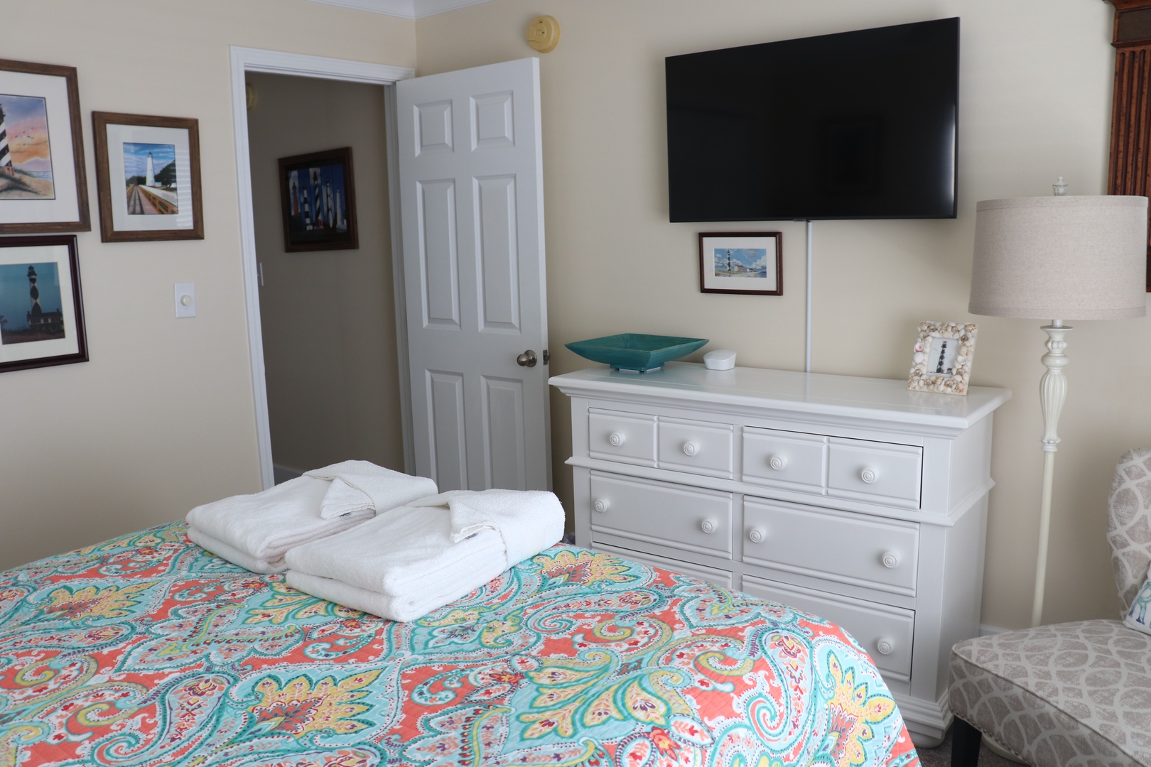 Relax in your cheerful bedroom with coastal artwork, plush towels, and modern amenities for your perfect getaway.