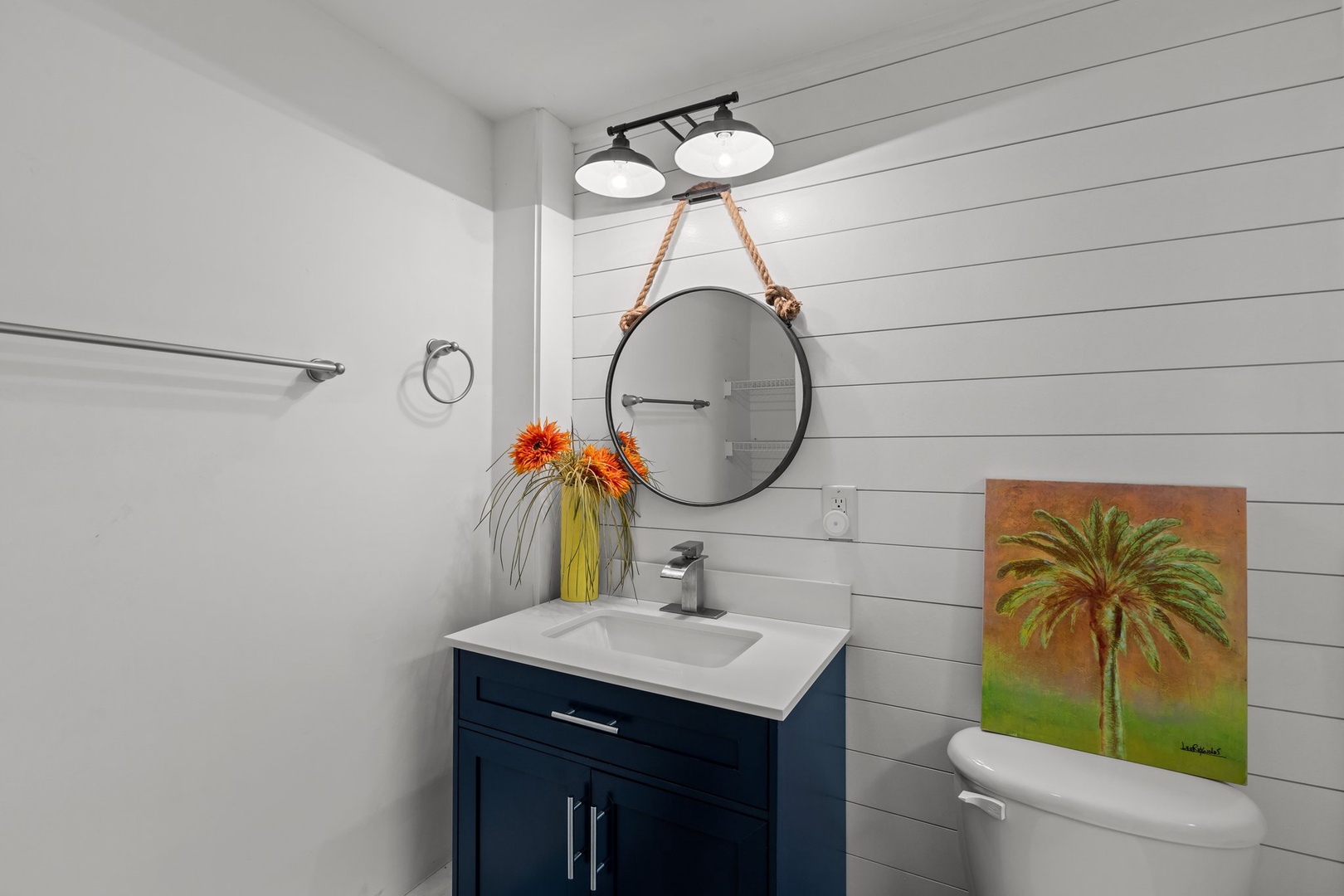 You'll love this stylish bathroom with its rope-framed mirror, modern navy vanity, and bright coastal charm - perfect for refreshing after beach days.