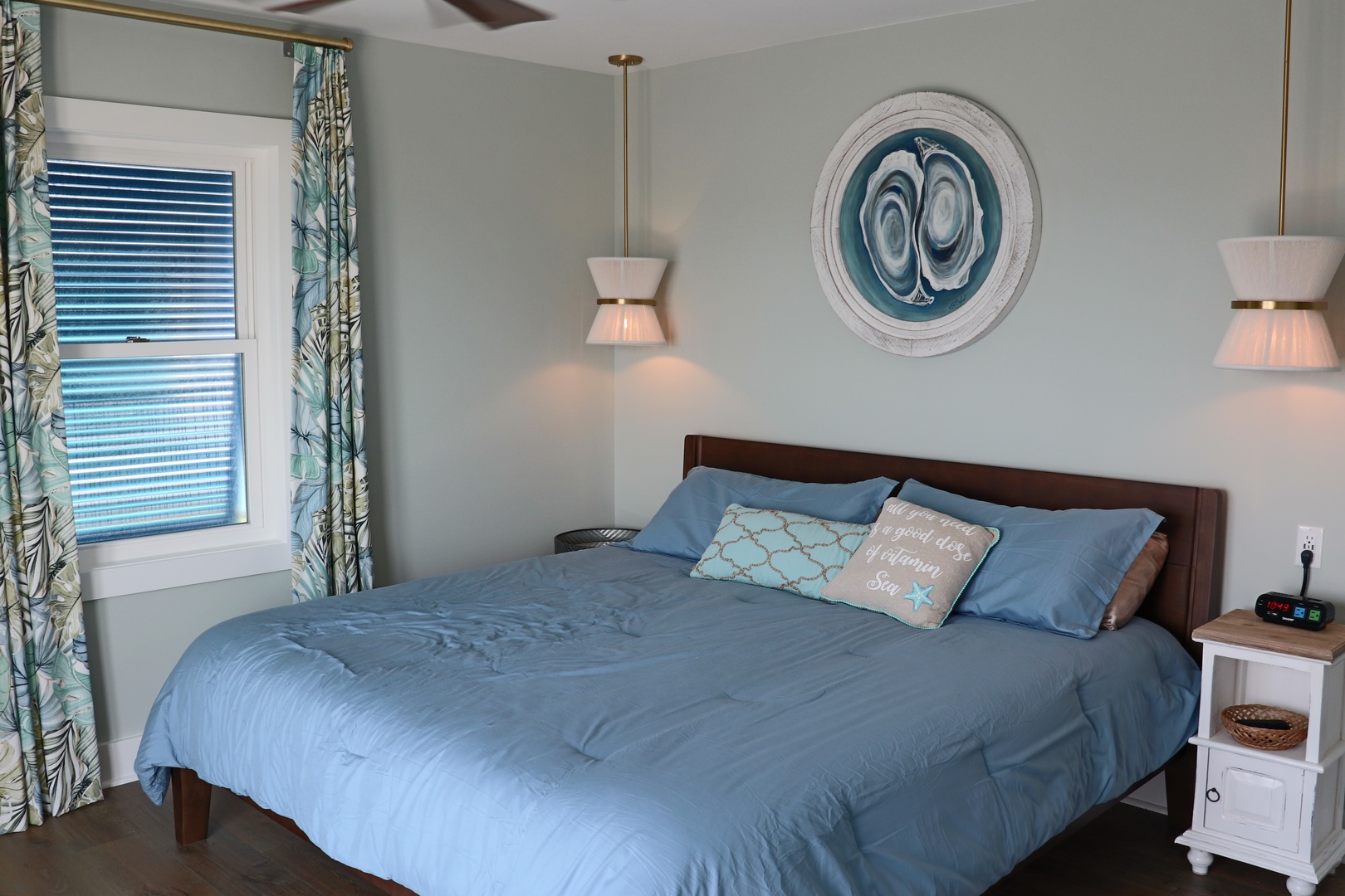 Drift off in this peaceful bedroom with coastal blue linens, warm pendant lighting, and tropical curtains creating your perfect retreat.