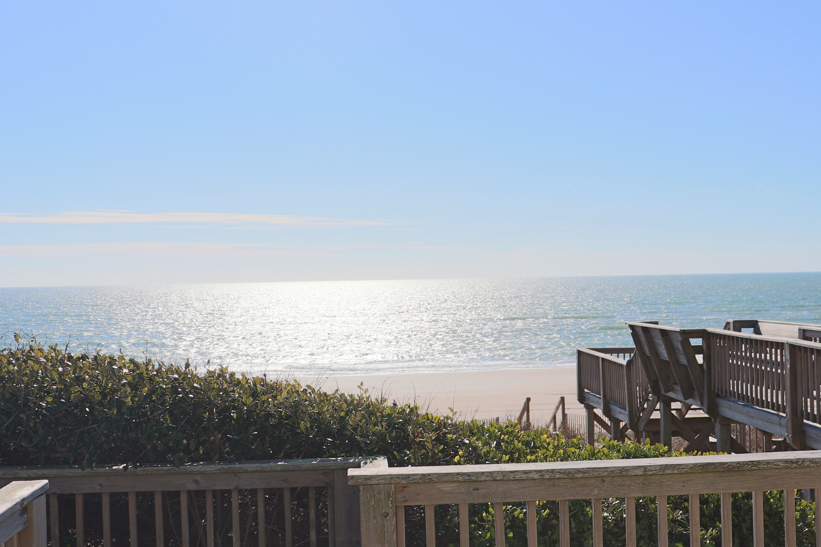 Wooden boardwalk leads to pristine beach with sparkling ocean waters and clear blue skies.