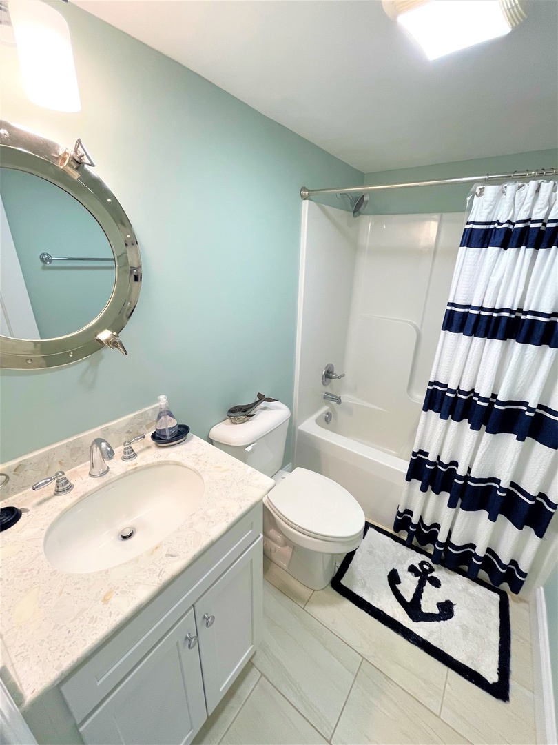 Step into your coastal-themed bathroom featuring a nautical porthole mirror and marble vanity. The spacious tub-shower combo offers relaxation after beach days.