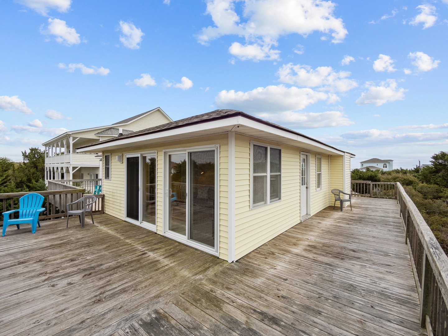 Beachside cottage with expansive wraparound deck offering panoramic views and bright blue Adirondack chairs for relaxing outdoors.