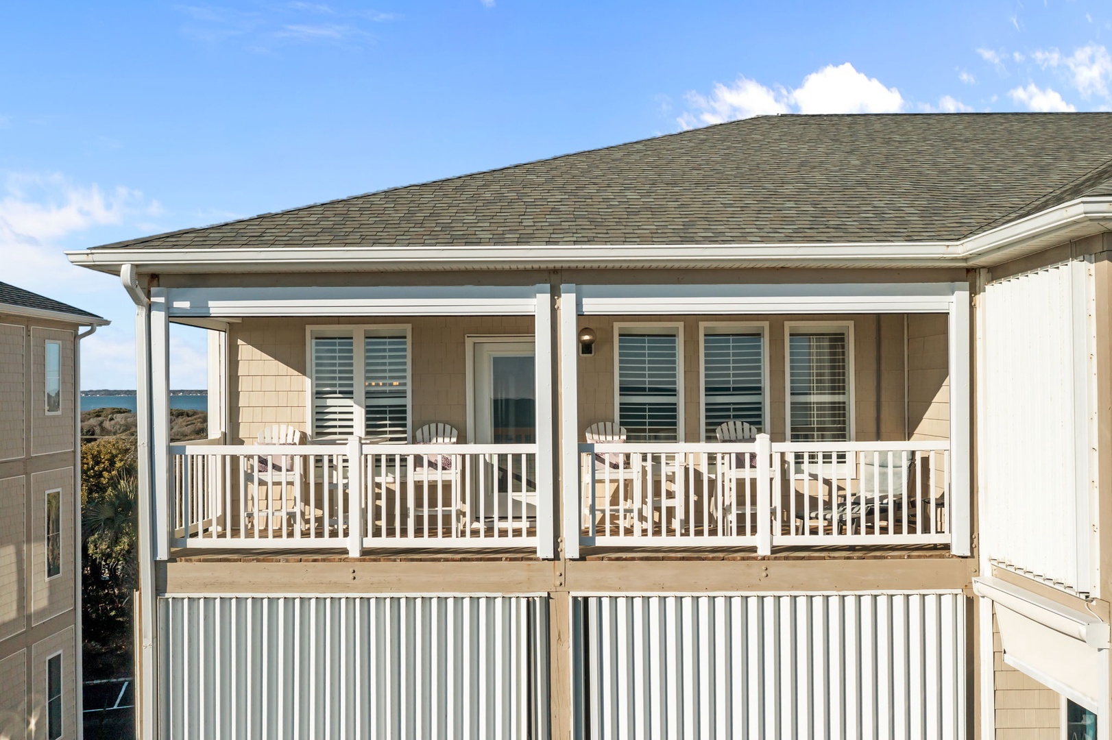 Coastal property featuring expansive covered deck with white railings and shuttered windows overlooking the oceanfront area.