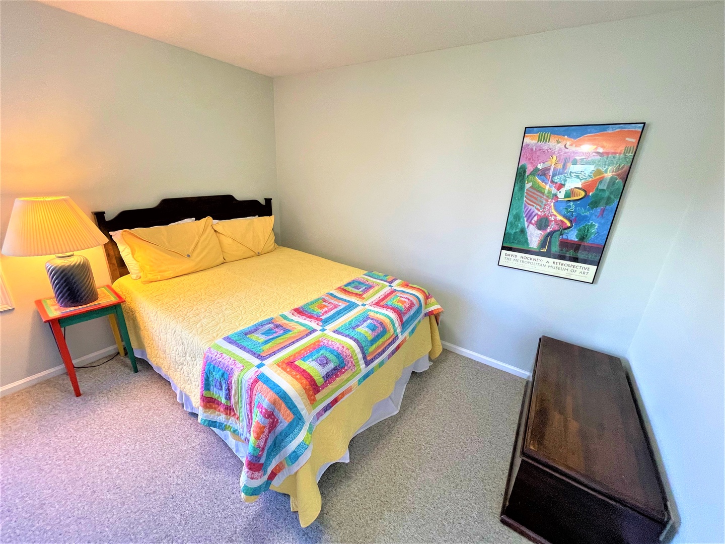 Unwind in your cozy bedroom featuring a comfortable queen bed with cheerful quilted throw and warm ambient lighting from the bedside table lamp.