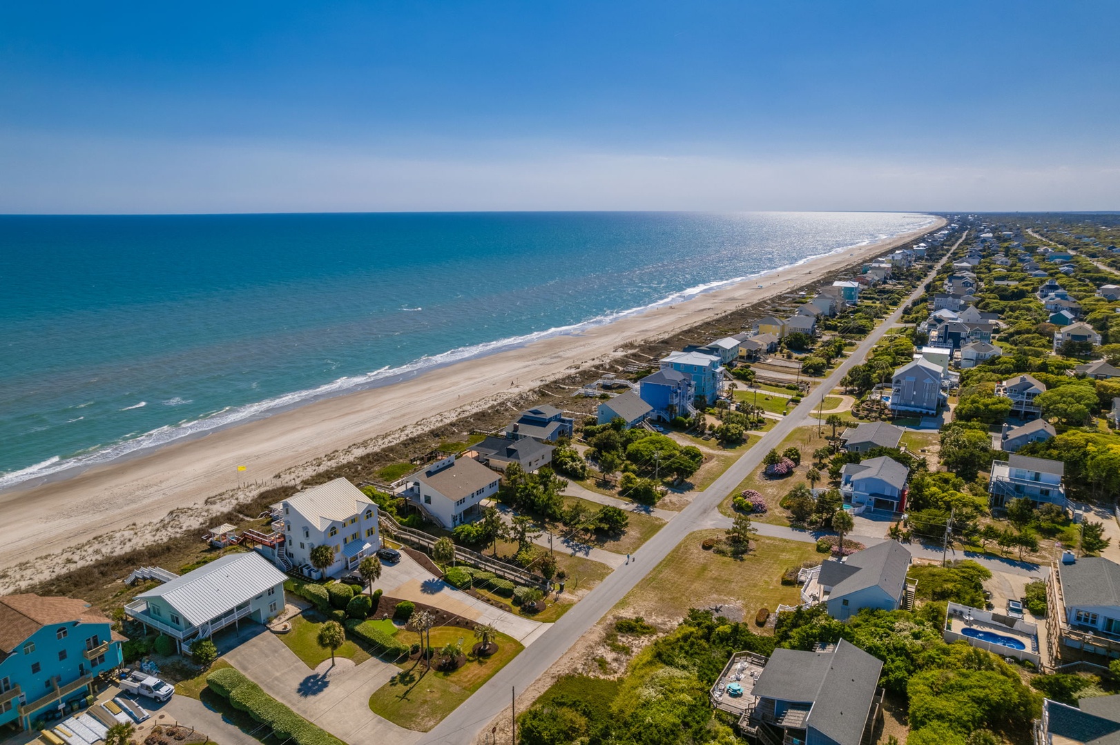 Stunning aerial view showcases beachfront vacation rental community with pristine sandy shores and turquoise waters stretching to the horizon.