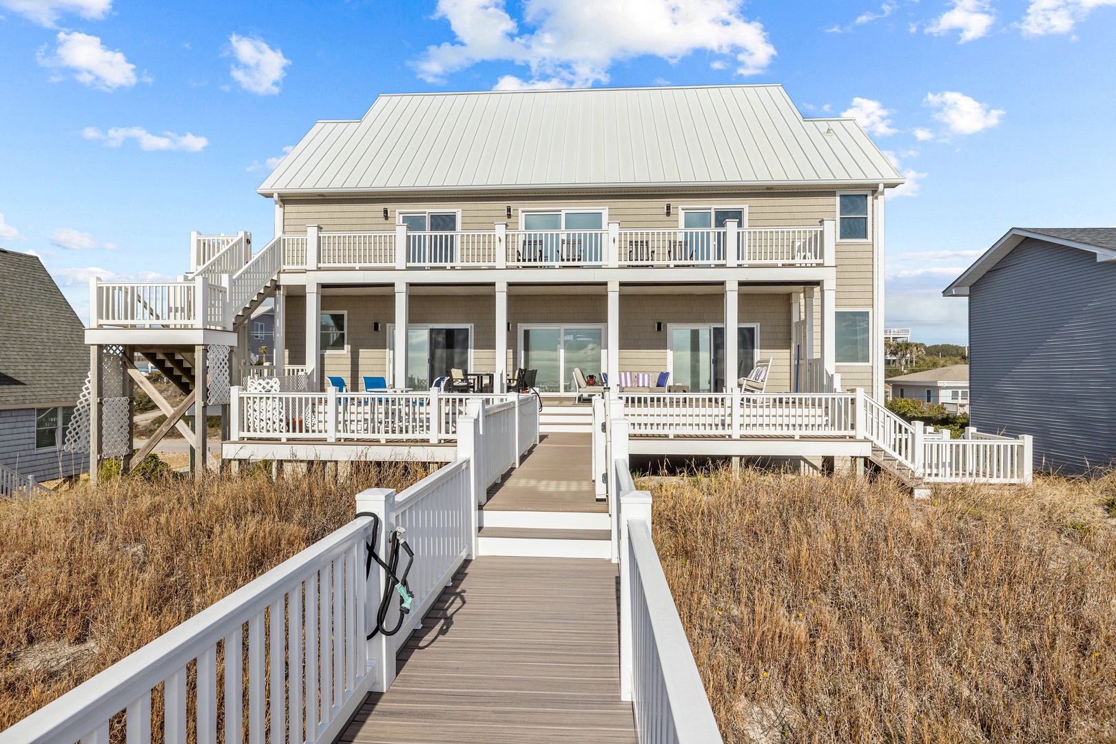 Coastal vacation home with boardwalk access through natural dunes, featuring multiple decks and panoramic views of the surrounding beach community.