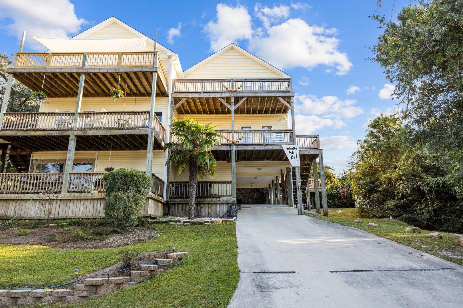 Modern beach house with spacious balconies and convenient driveway parking surrounded by lush tropical landscaping.