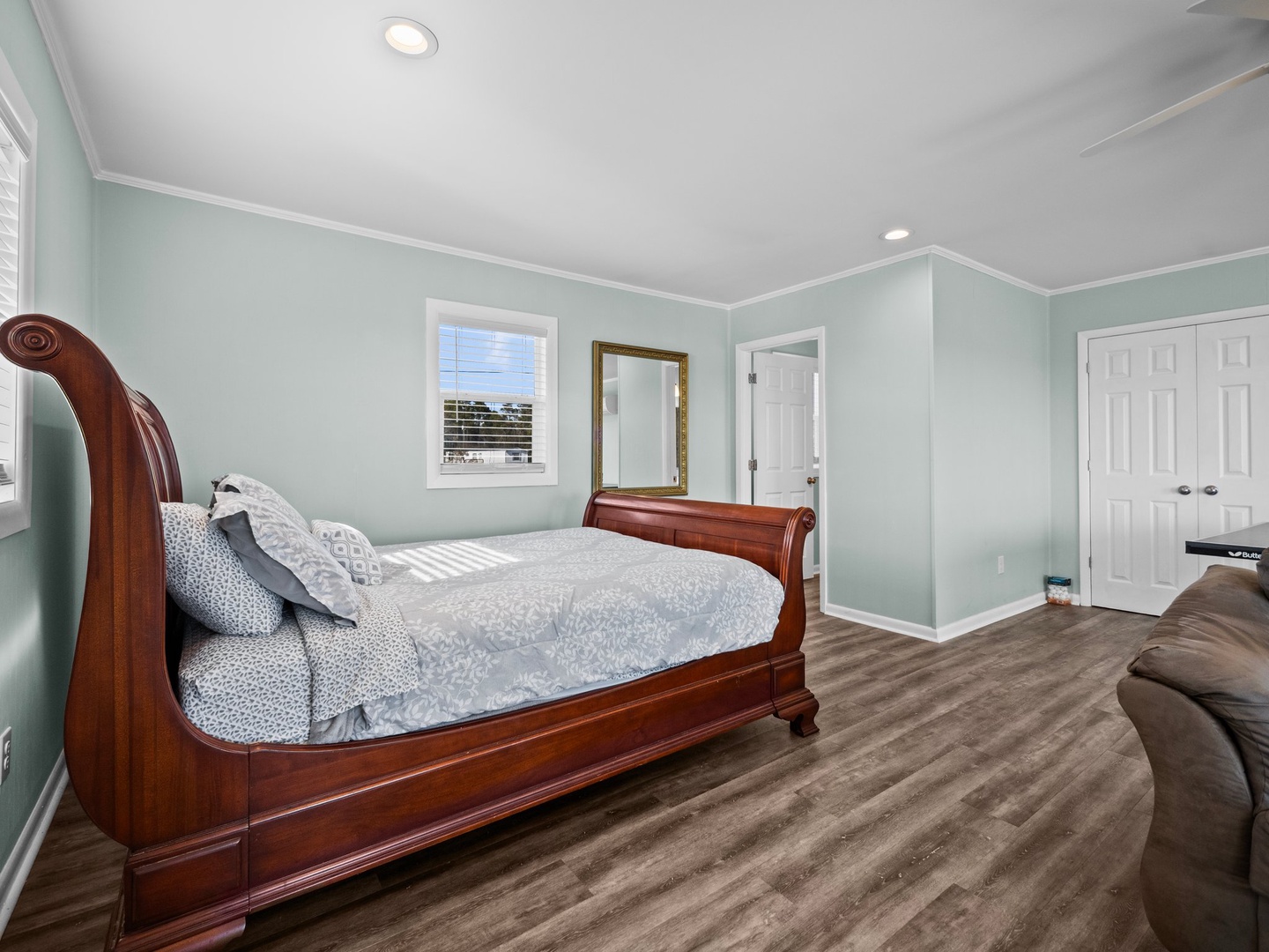 Unwind in your serene bedroom with soothing mint walls, elegant mahogany furniture, and soft natural light streaming through pristine windows.