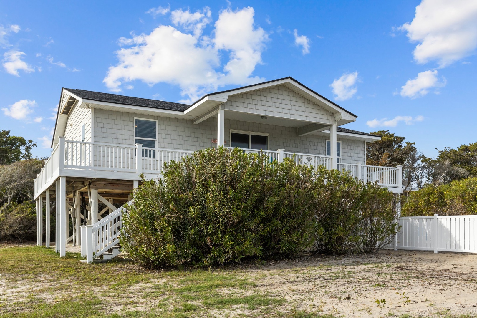 Elevated coastal cottage featuring wraparound deck and natural landscaping under bright blue skies.