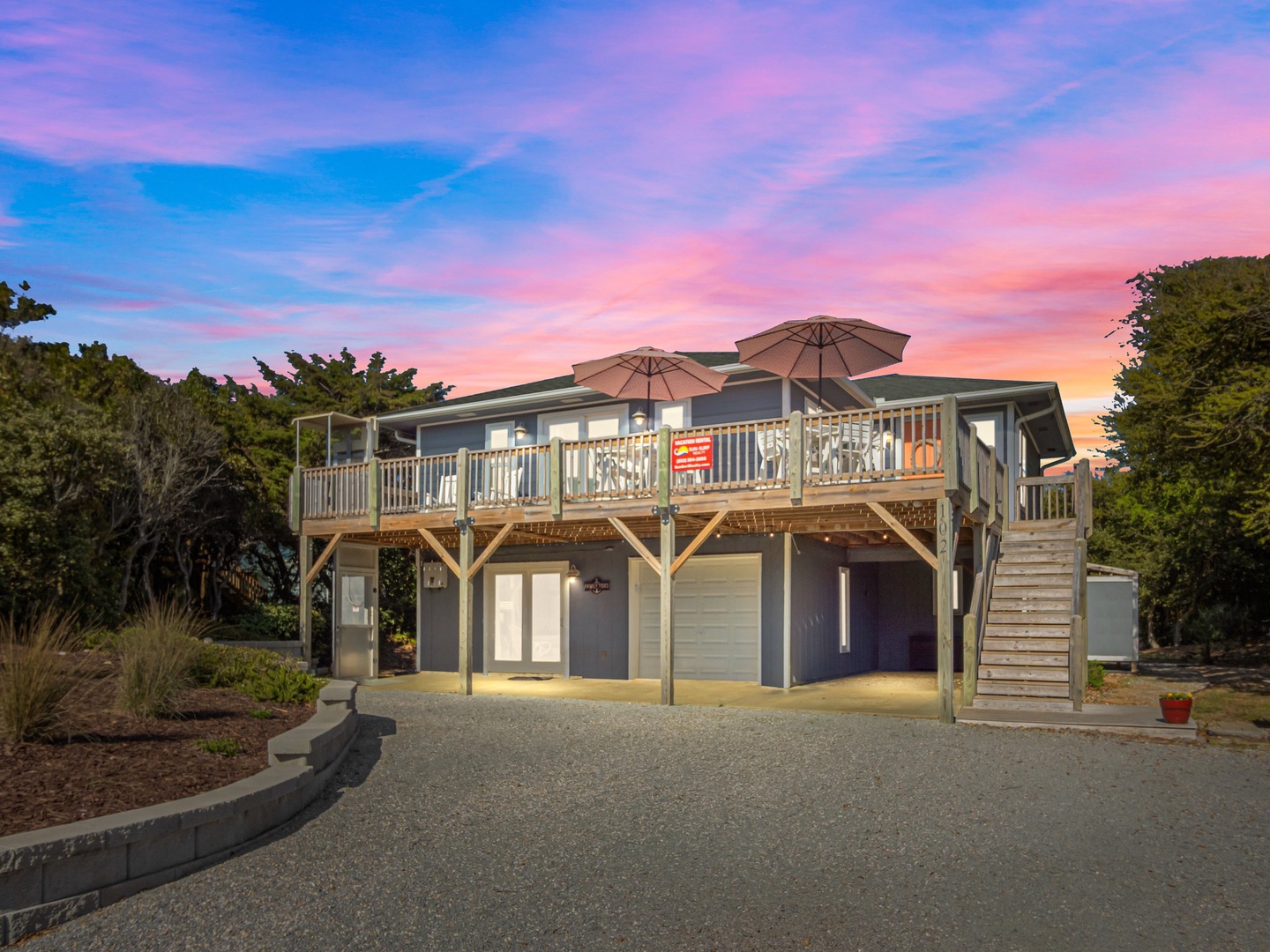 Modern beach house with elevated deck and umbrellas overlooking spectacular sunset views in a peaceful coastal setting.