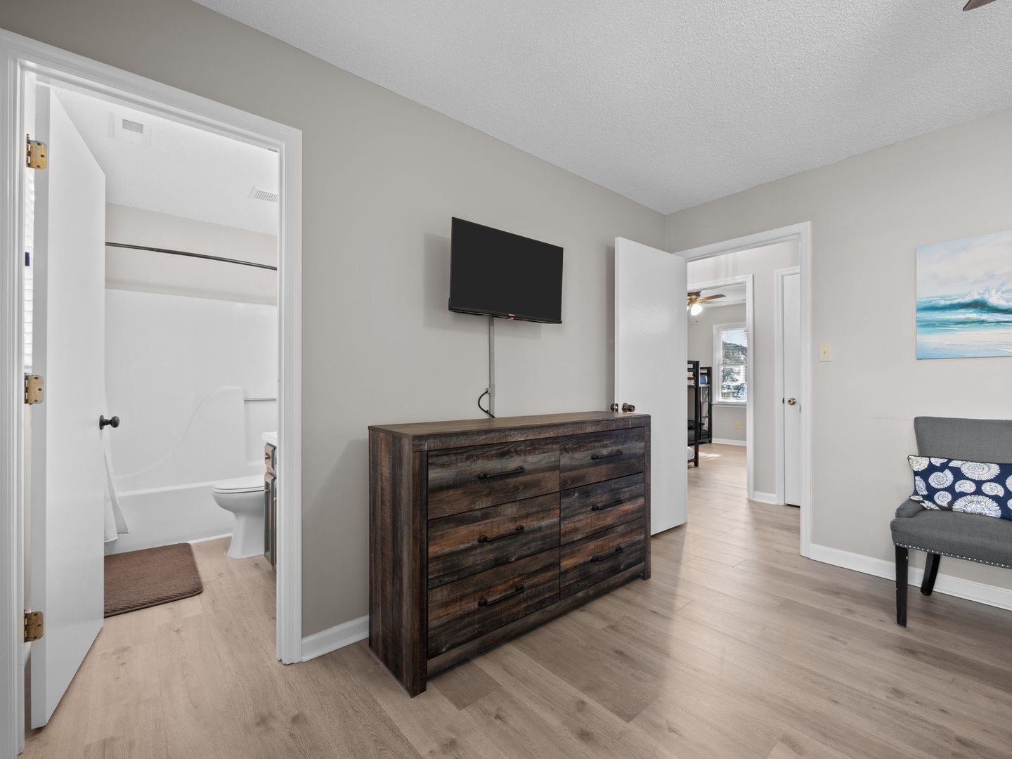 Your bedroom features a wall-mounted TV and rustic dresser, with an en-suite bathroom and coastal artwork creating a relaxing retreat.