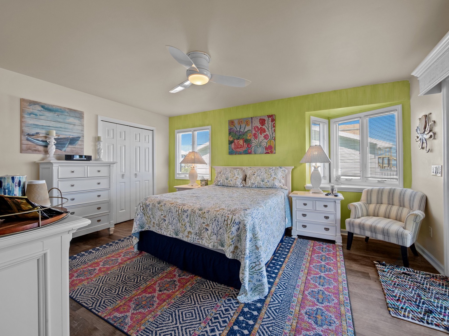 Your bright bedroom features a cozy bed, cheerful green accent wall, and comfortable seating area perfect for relaxing after beach adventures.