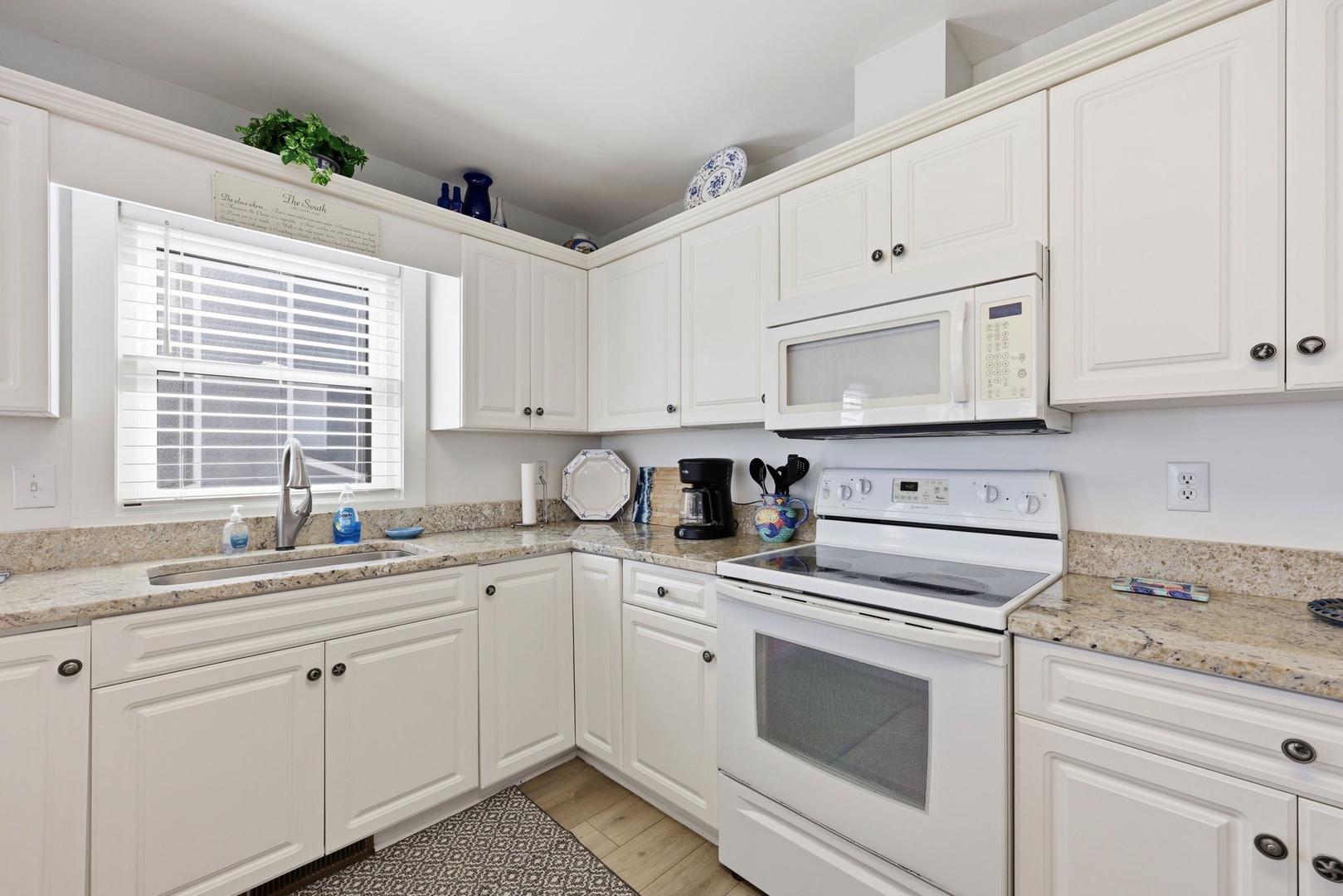 Your fully equipped kitchen invites easy meal prep with granite countertops, white cabinetry, and modern appliances bathed in natural light from the window.
