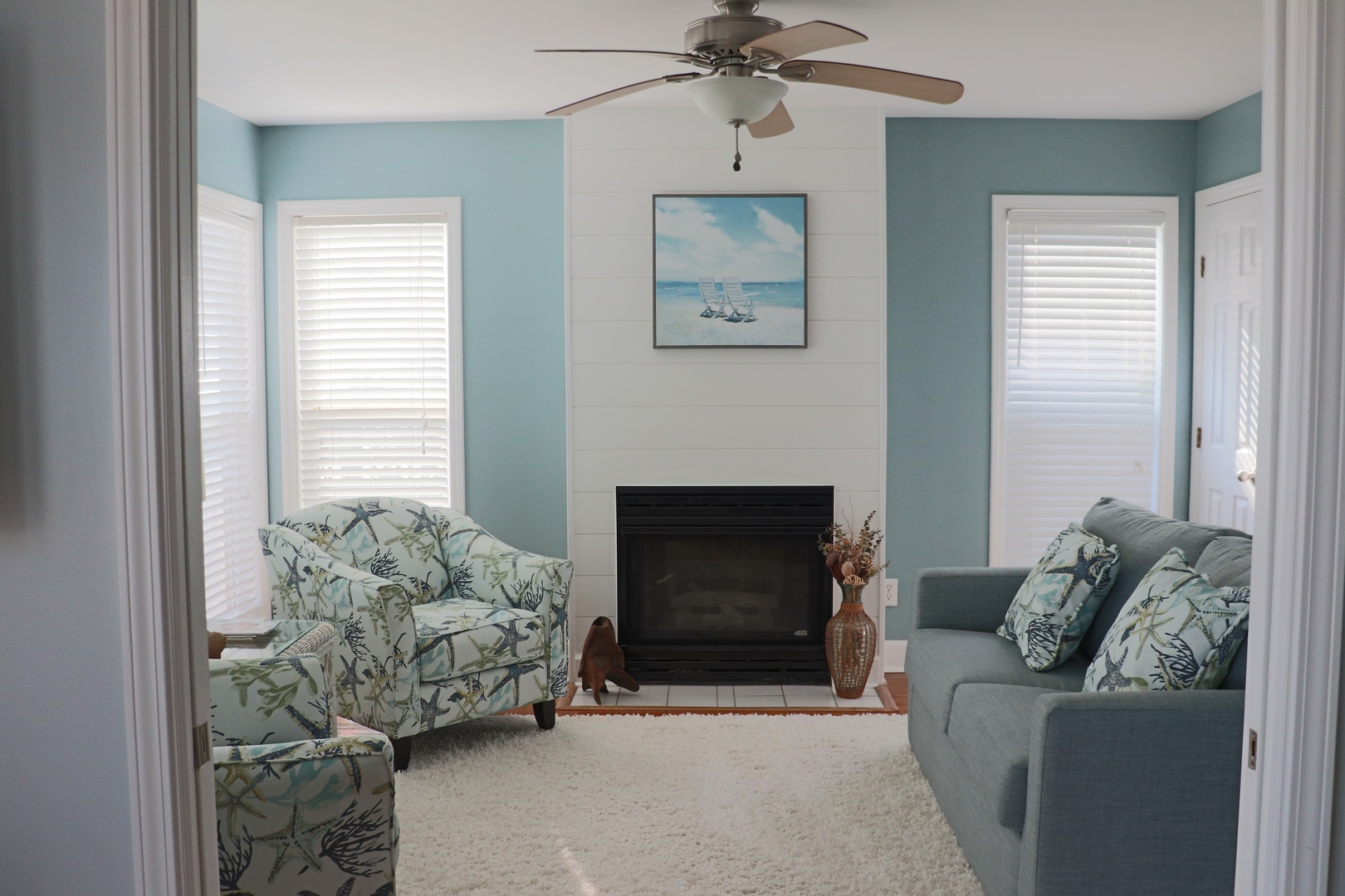 Unwind in your serene coastal living room with ocean-themed decor, comfy seating, and a cozy fireplace for perfect relaxation.