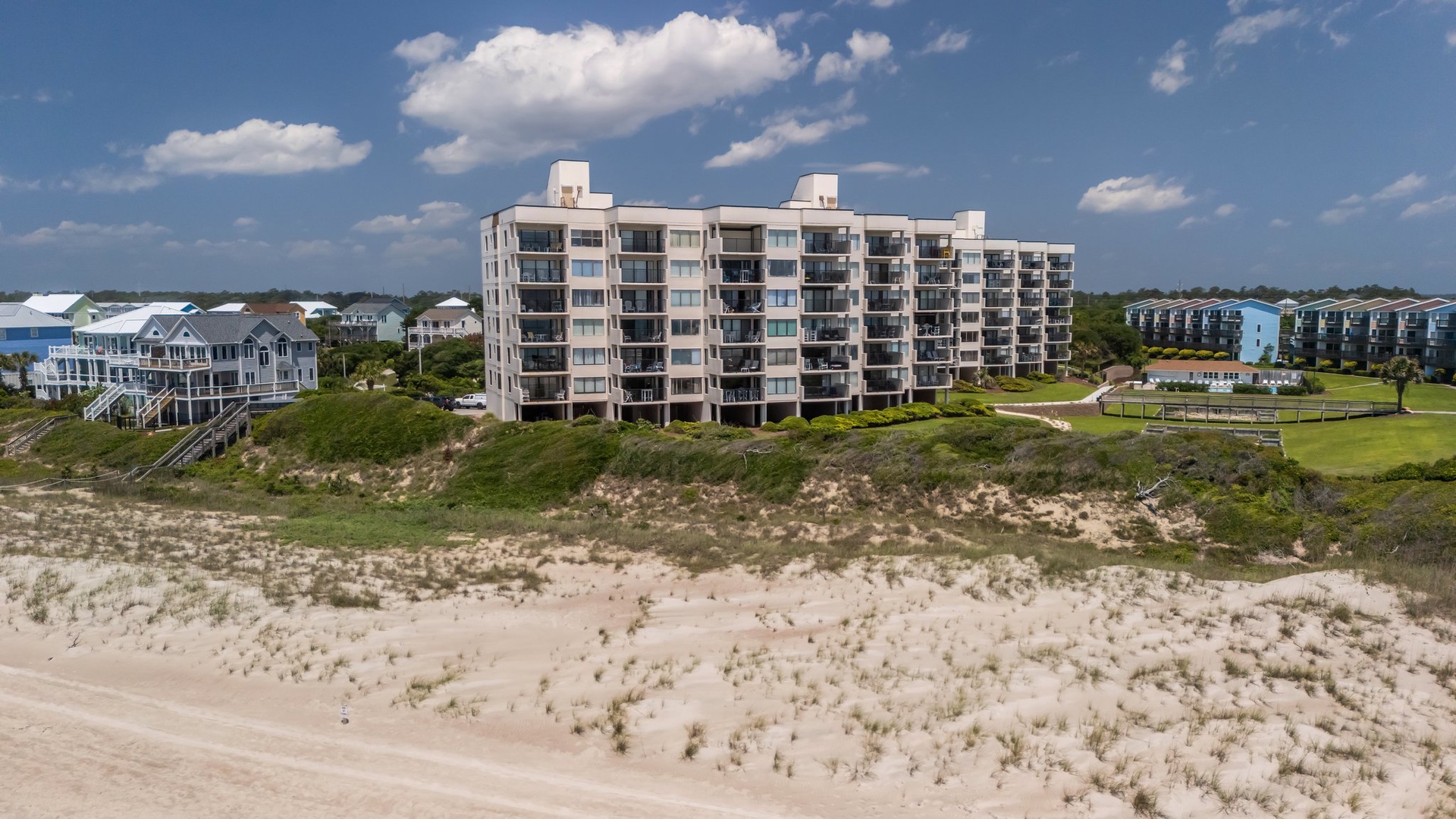Beachfront condominium complex situated directly on pristine sandy shores with natural dune vegetation and nearby residential properties.