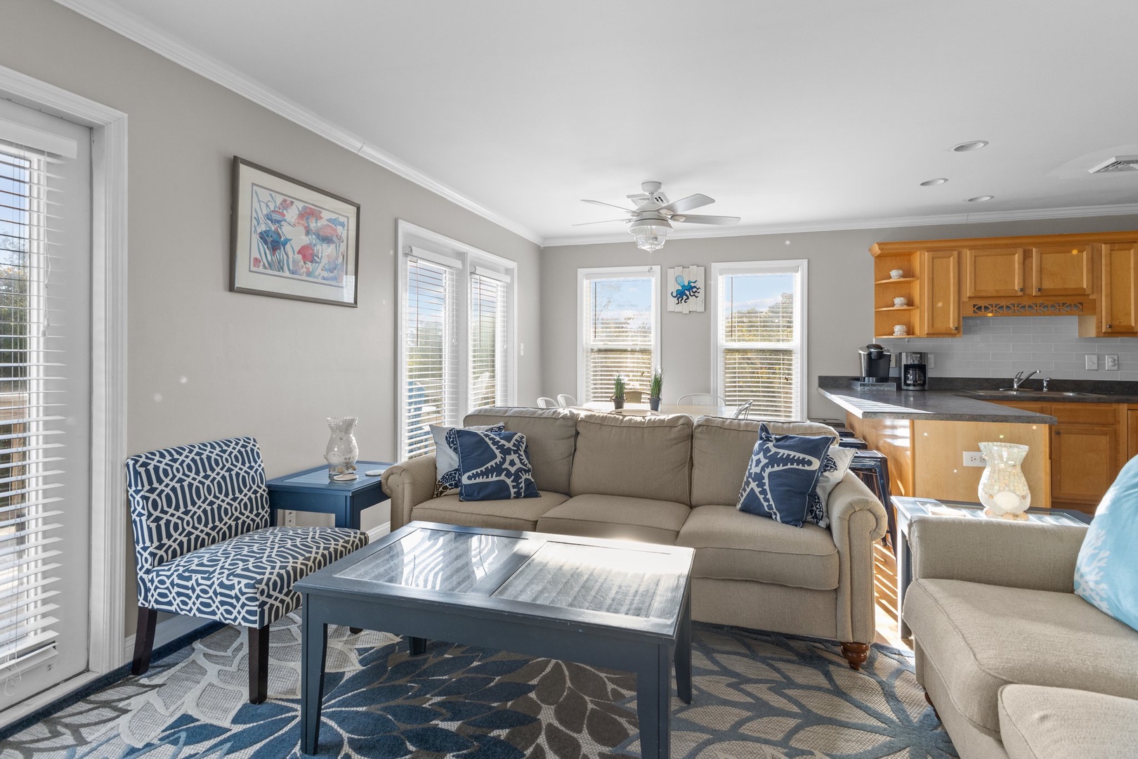 Relax in your bright living space with comfortable seating, modern kitchen access, and natural light streaming through large windows.