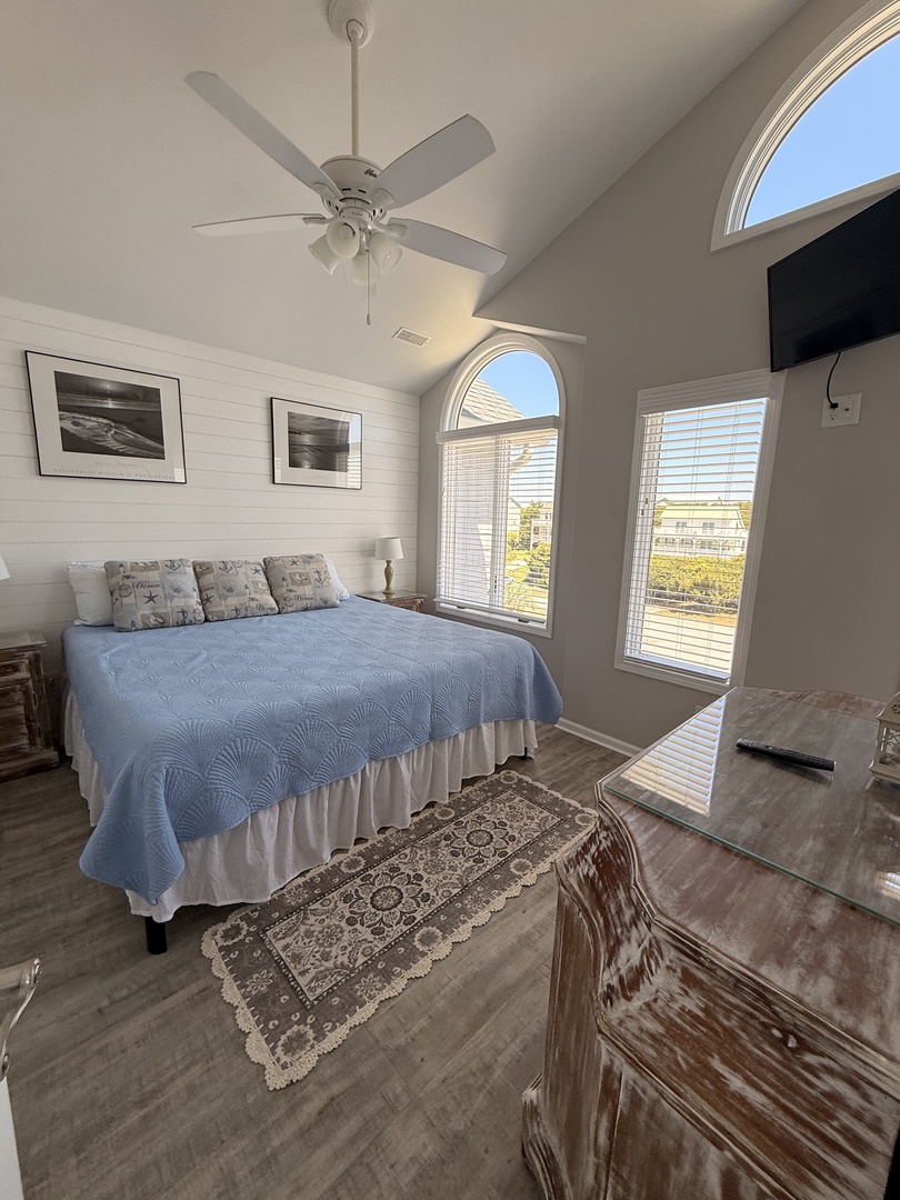 Sunlight pours through skylights, illuminating your cozy bedroom retreat with soft blue linens, a ceiling fan for comfort, and charming artwork—your peaceful escape awaits.