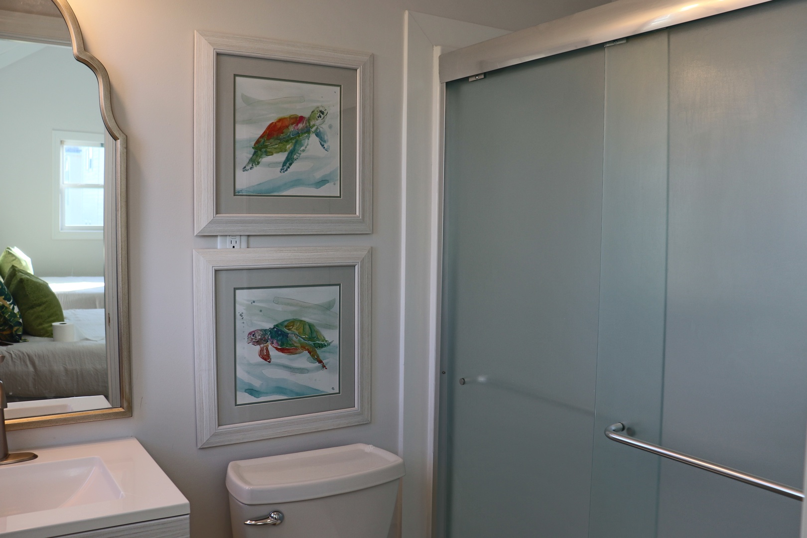 Your private bathroom features a sleek frosted glass shower, charming sea turtle artwork, and thoughtful coastal touches that make getting ready feel like a spa retreat.
