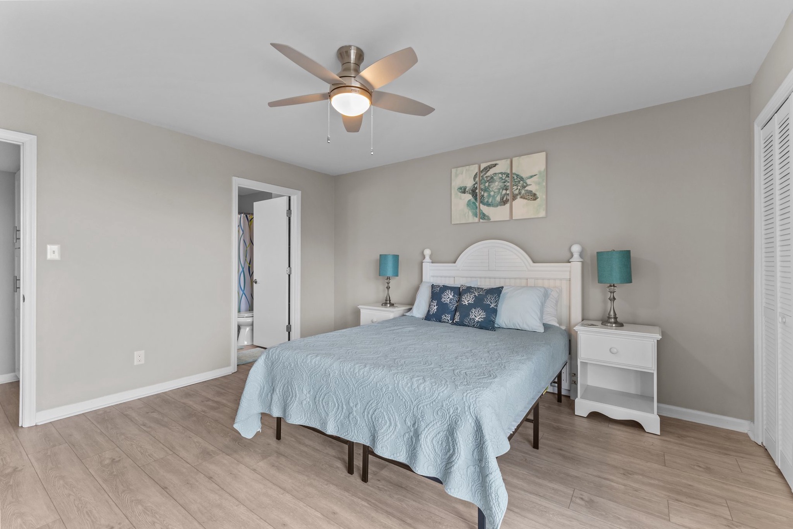 Drift into peaceful sleep in your coastal-themed bedroom with soft blue linens, gentle ceiling fan, and charming sea turtle artwork overhead.