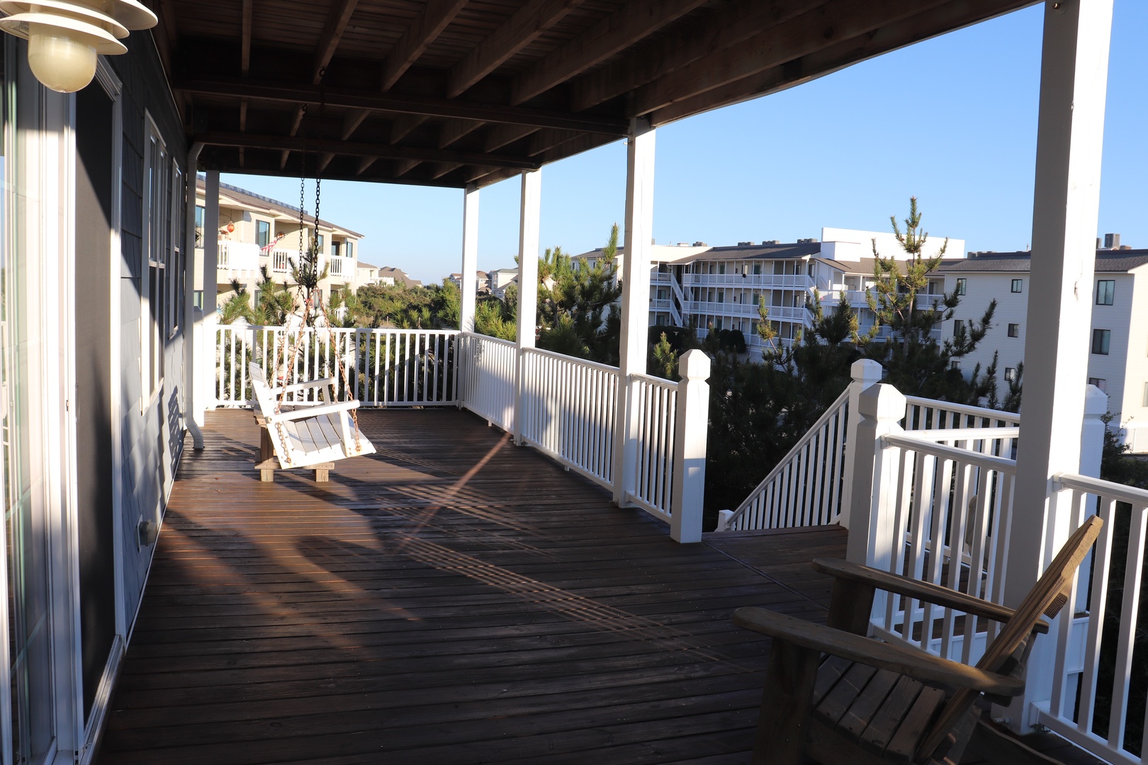 Sip your morning coffee on this expansive covered deck, where white railings frame peaceful neighborhood views and gentle ocean breezes create the perfect retreat.