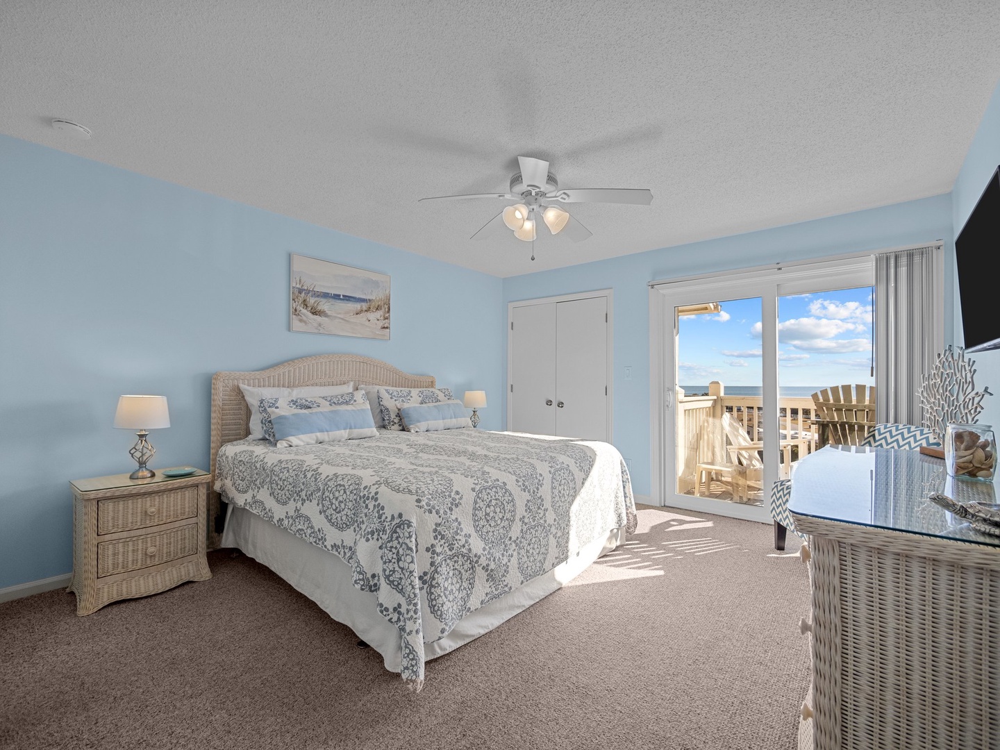 Wake to ocean breezes in your serene blue bedroom, where coastal charm meets comfort with wicker furniture and private balcony access.